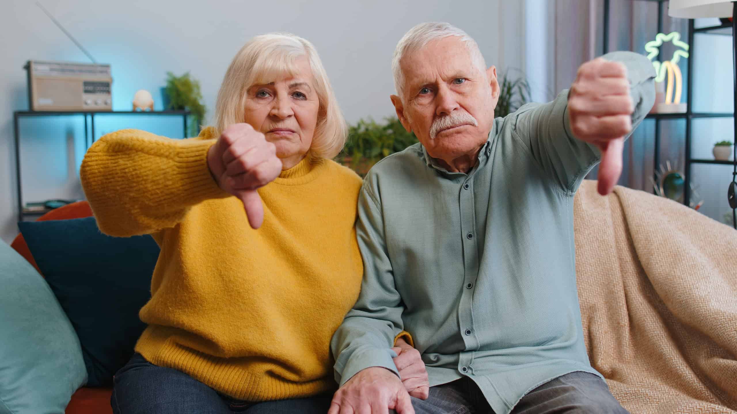 Dislike. Upset senior family grandparents man woman showing thumbs down sign, expressing discontent, disapproval, dissatisfied bad work at home. Displeased old grandmother, grandfather couple on sofa