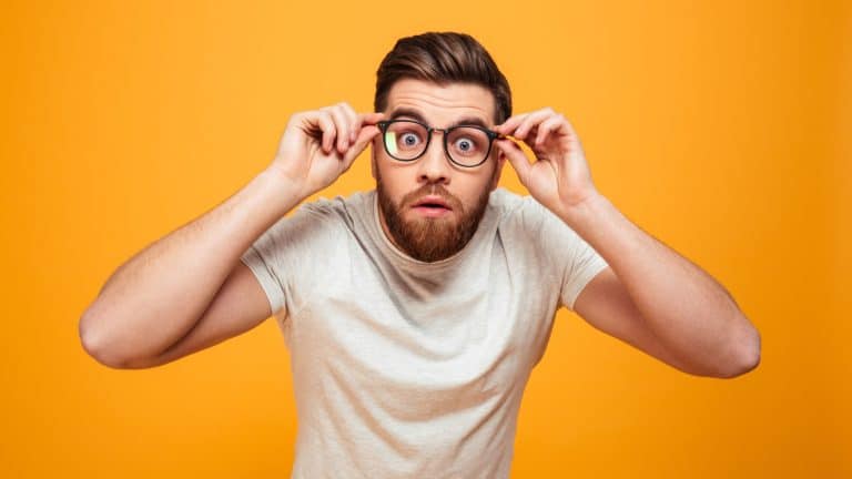 Portrait of a shocked bearded man in eyeglasses looking at camera isolated over yellow background