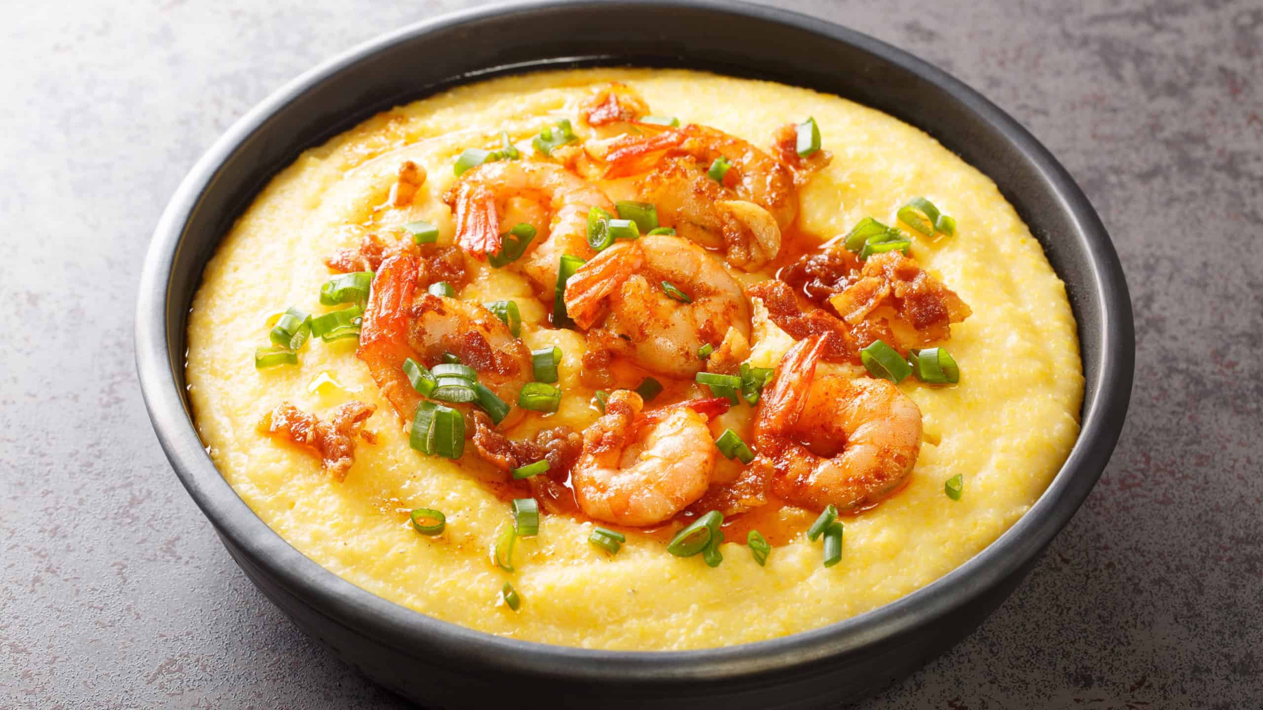 Delicious yellow grits with cheese, shrimps and bacon close-up in a plate on the table. horizontal