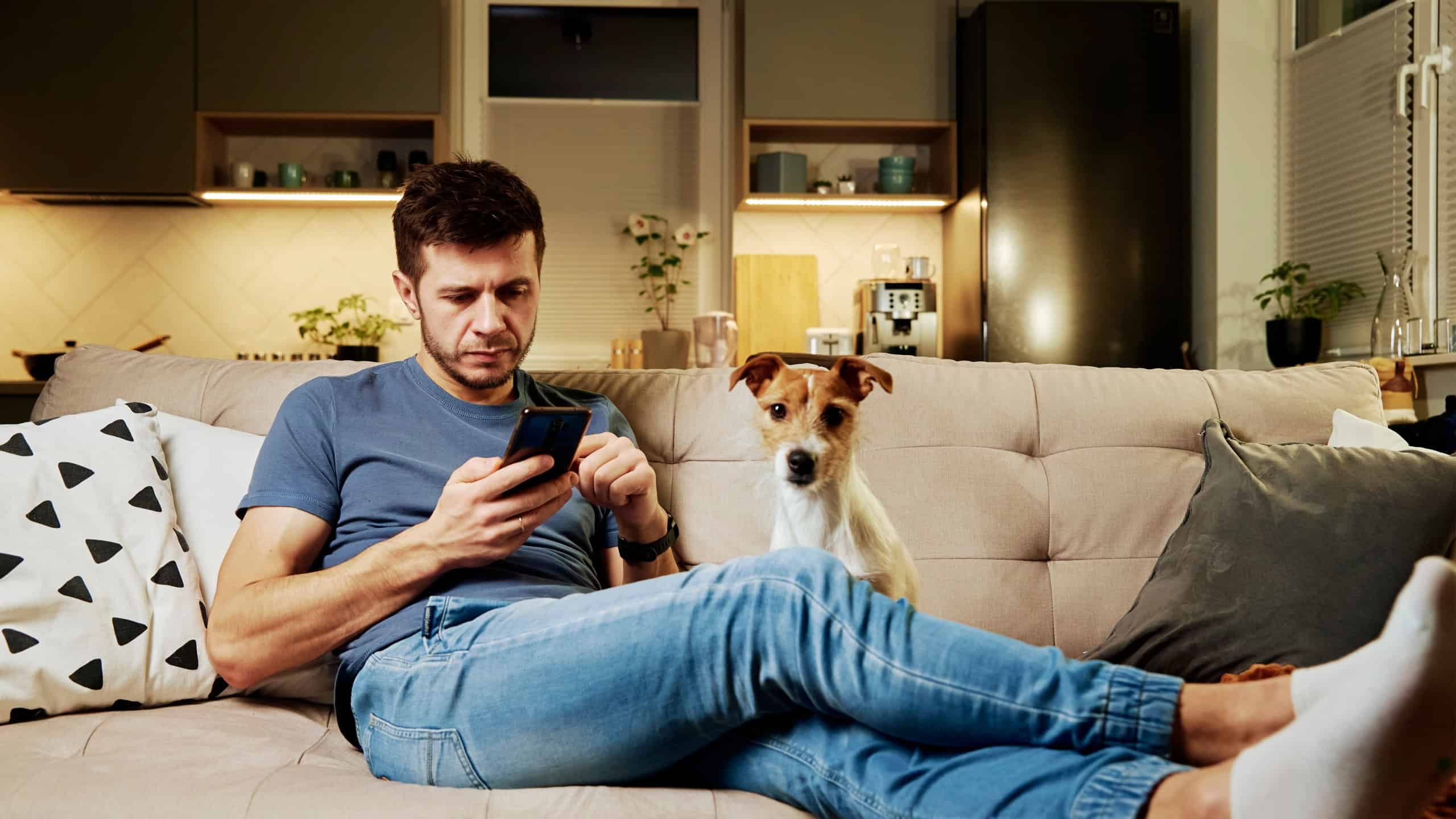 Man resting on sofa with her dog and using smartphone