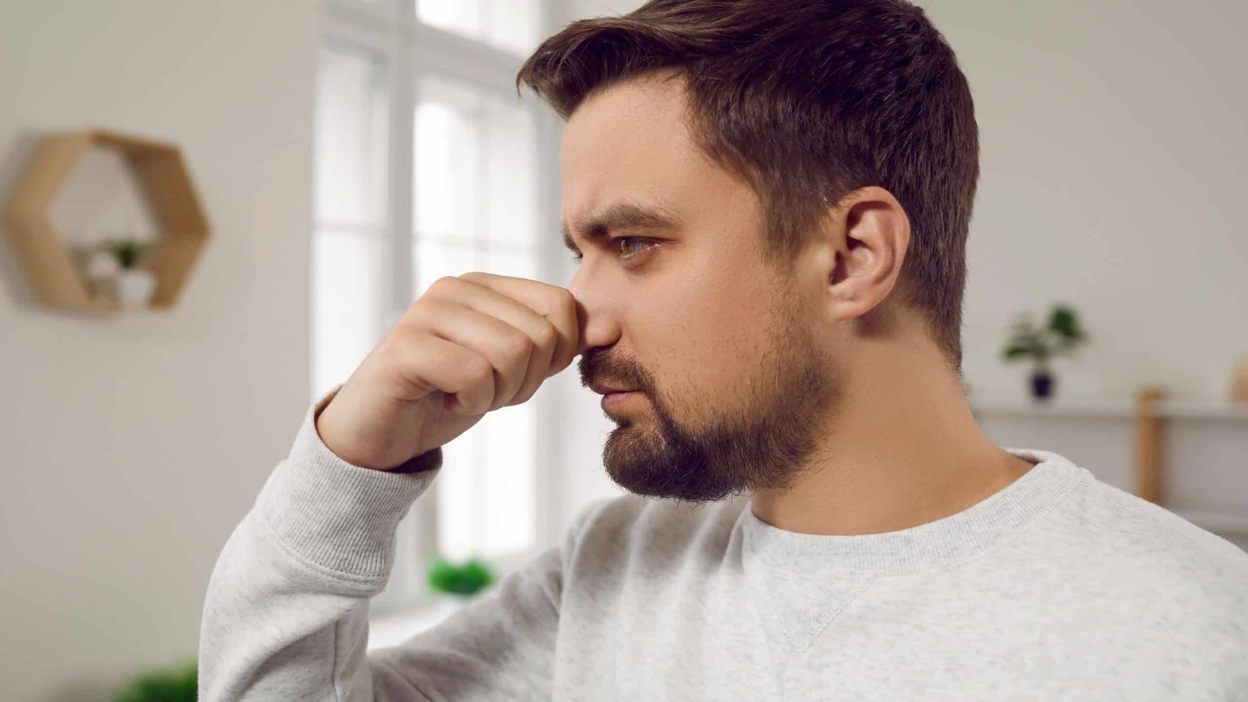 Man smells something bad at home. Young man pinches his nose as he feels a bad, unpleasant smell of something stinking in the house. Close up shot