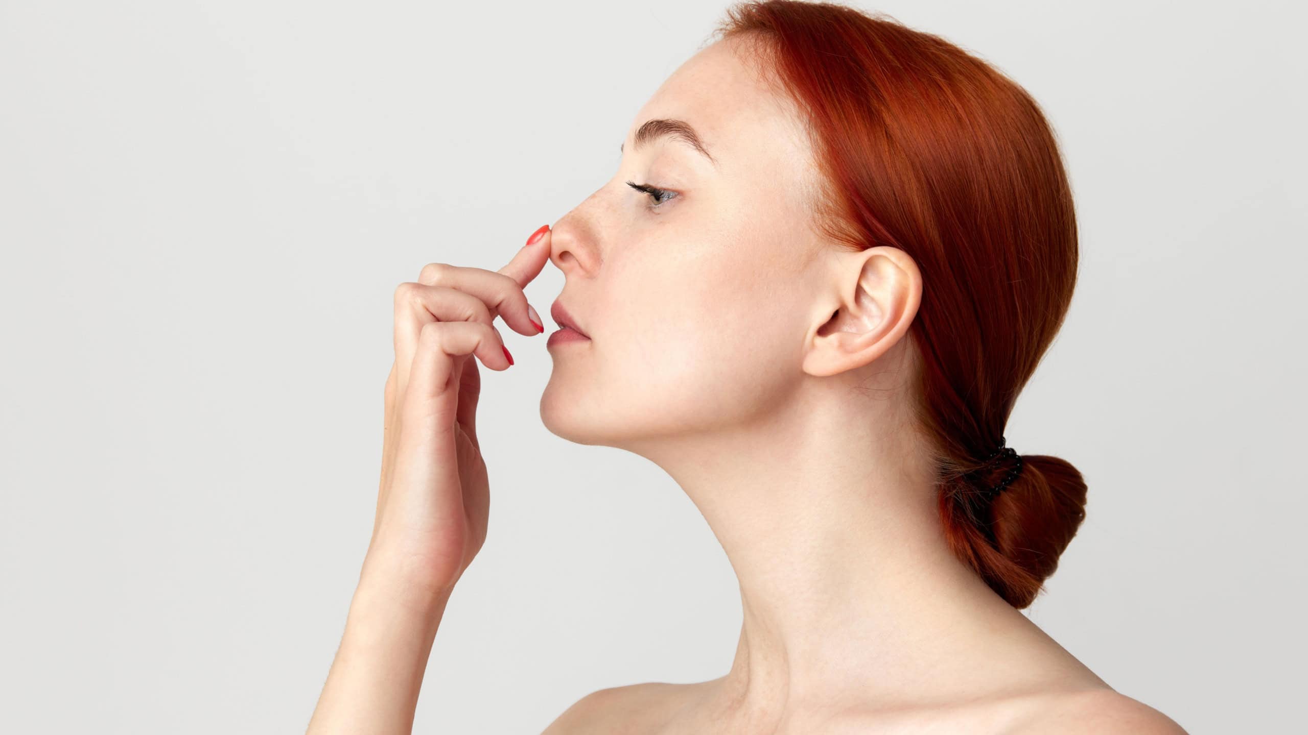 Profile view of young redhaired woman with bared shoulders touching her nose with finger. Rhinoplasty, plastic surgery, beauty standards, beauty, treatment, ad concept
