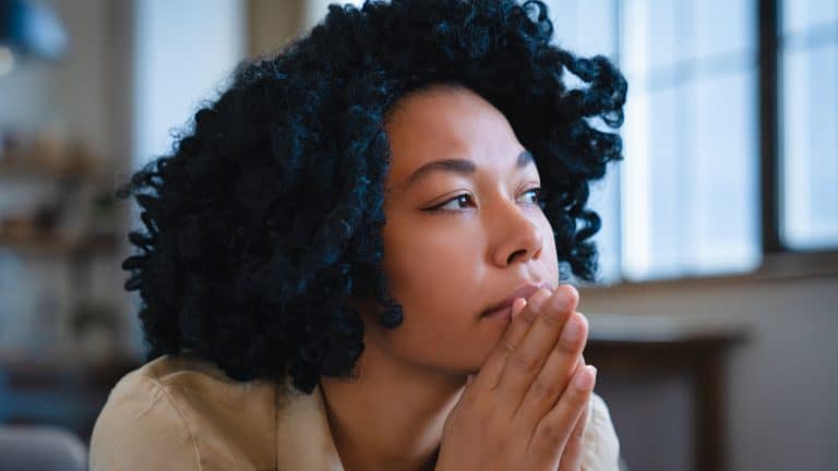 Discouraged pensive African American woman looking into distance thinking about ways to solve financial problems. Frightened black girl sits on sofa in living room having lost mood due to inflation