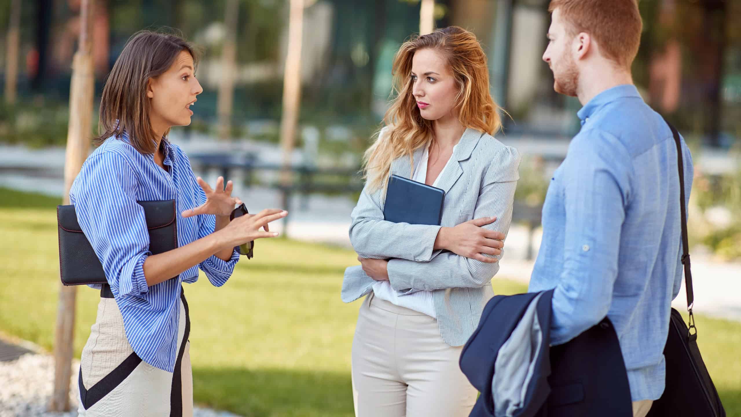 group of businesspeople, two female and one male, outdoor talking. One female explaining and gesture to her colleagues, business partners