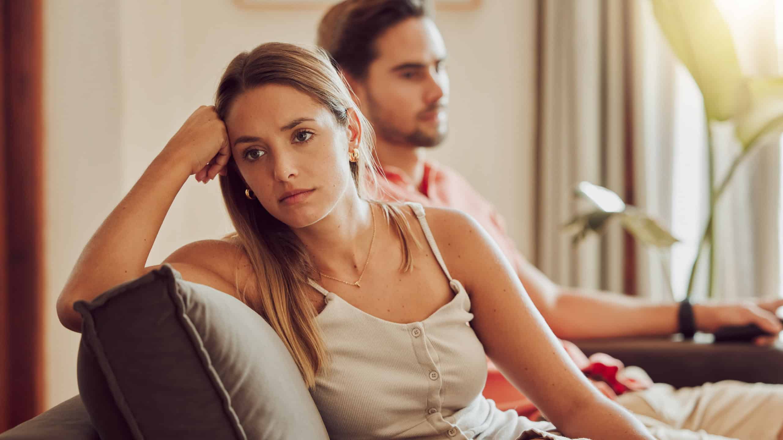 Unhappy, sad and annoyed couple after a fight and are angry at each other while sitting on a couch at home. A woman is stressed, upset and frustrated by her boyfriend after an argument