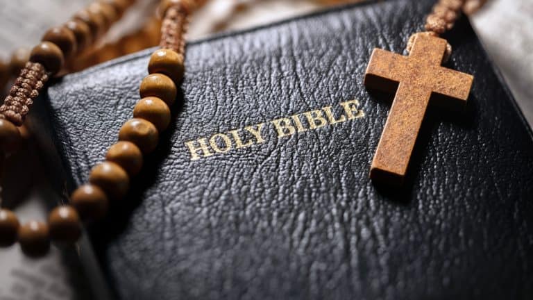 Praying with wooden rosary beads crucifix cross on Holy Bible study background