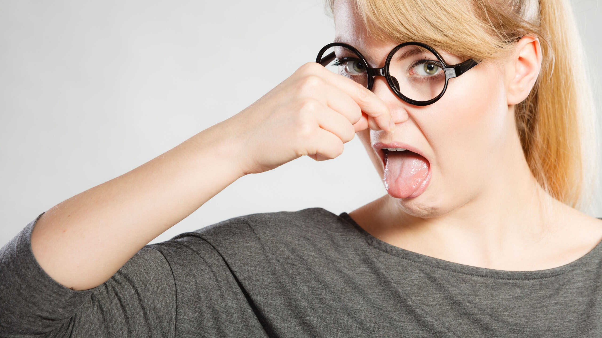 Filth hygiene dirt trash garbage concept. Nerdy girl holding nose. Young blonde in glasses pinching to stop odor. Bad disgusting smell.