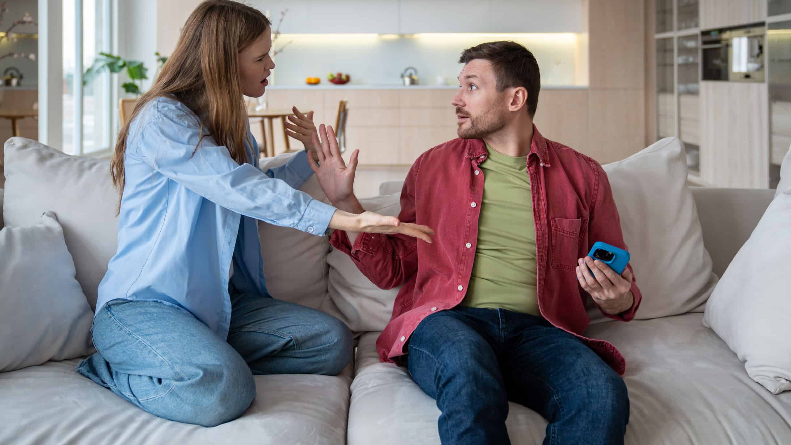 Jealous, incredulous man, suspecting betrayal treason, took smartphone from alarmed woman at home. Difficulty clarifying conflicting relationships in couple. Wife asks to respect personal boundaries.