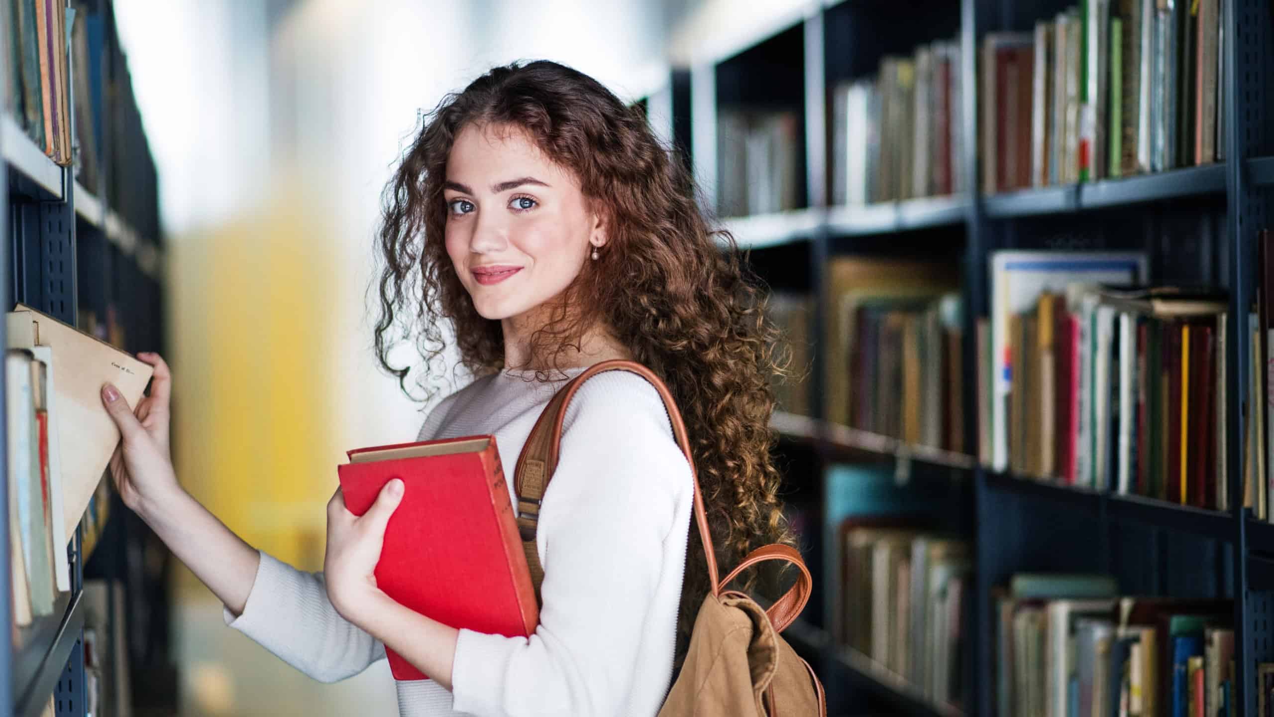 Young female student in library, looking for books, preparing for final exam.