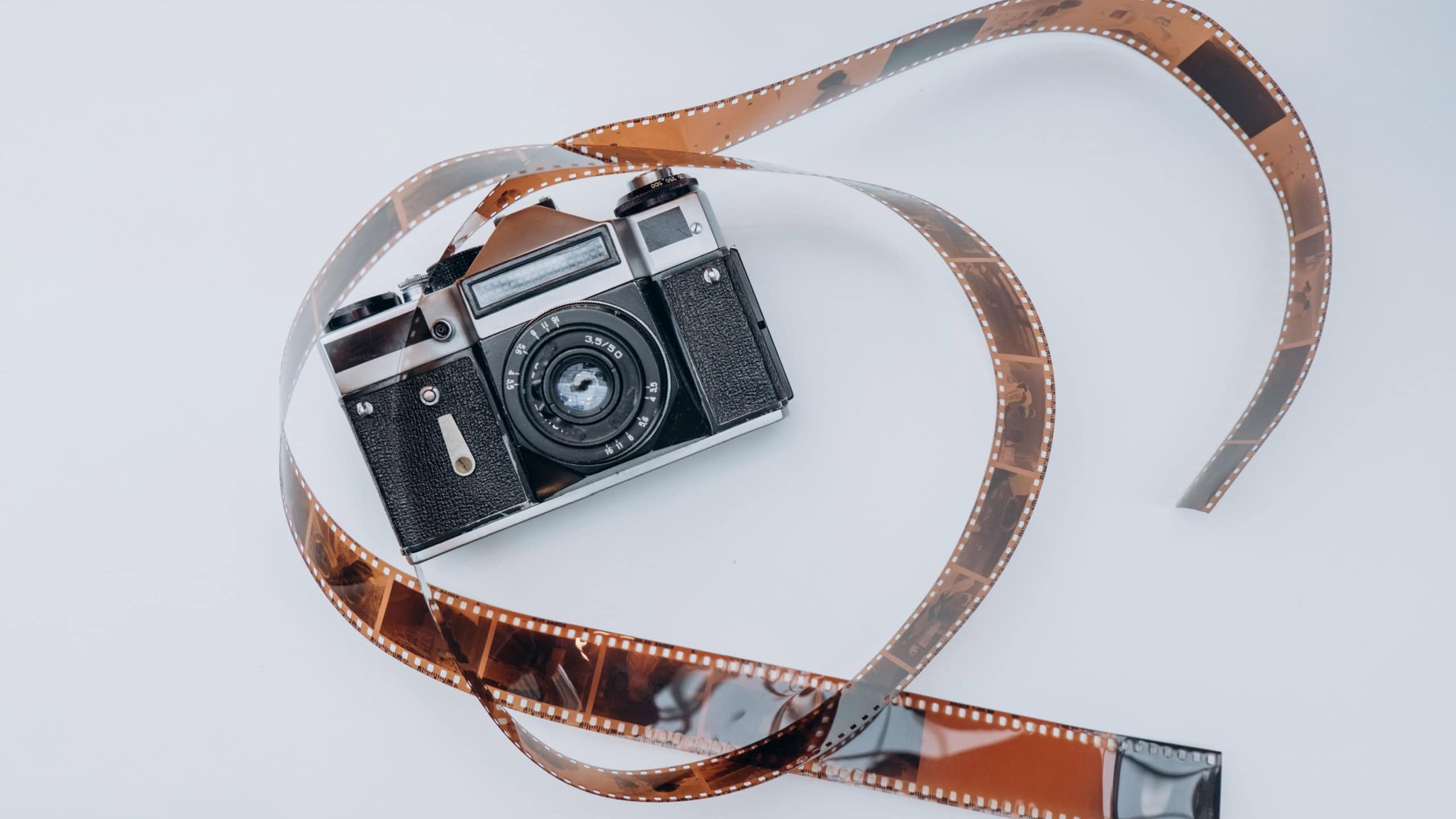 Vintage film camera with rolled 35mm film negative on white background, retro photography concept, analog camera and film strip
