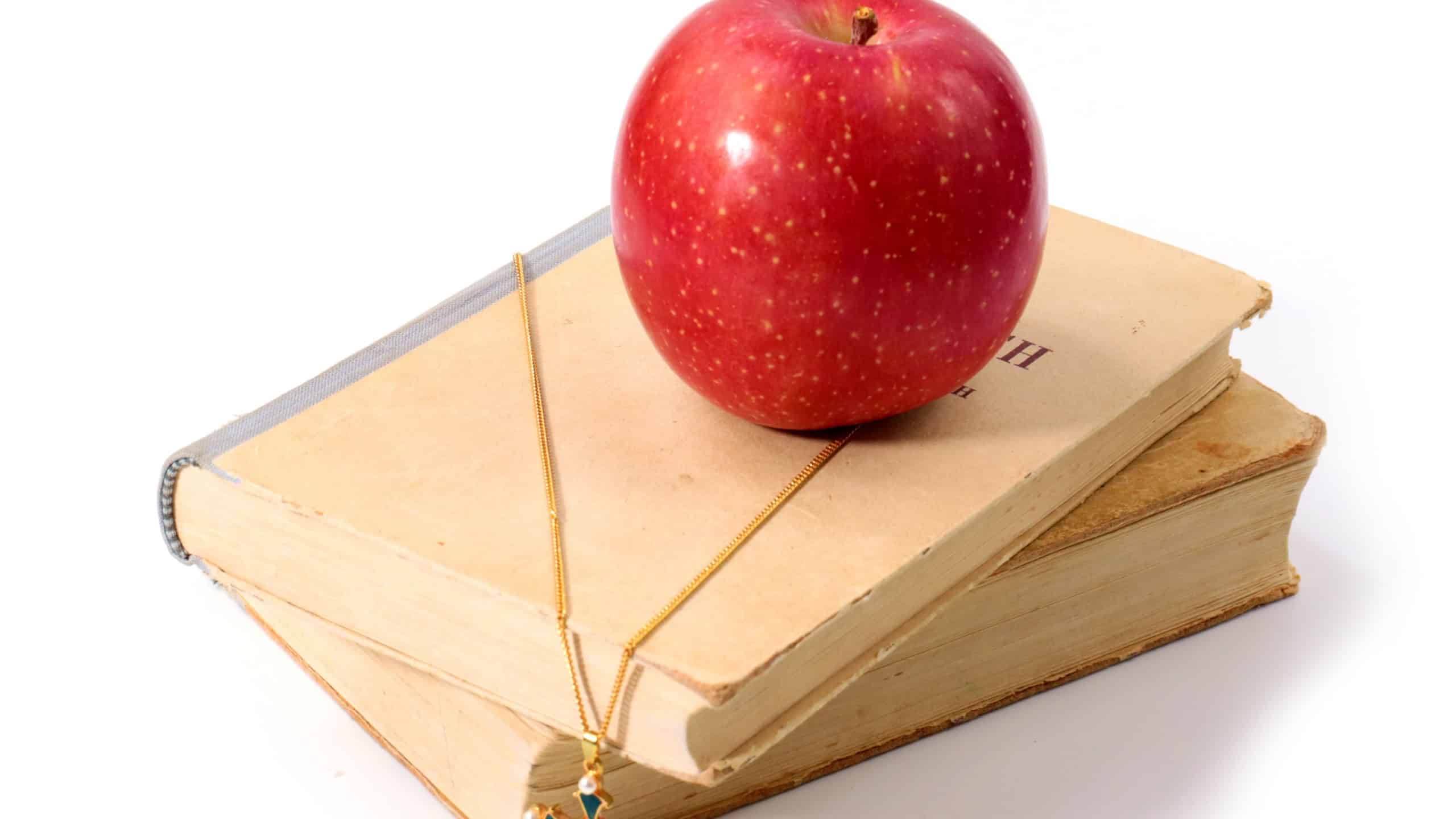 a beautiful ripe red apple on an old book and a Christian jewelry cross