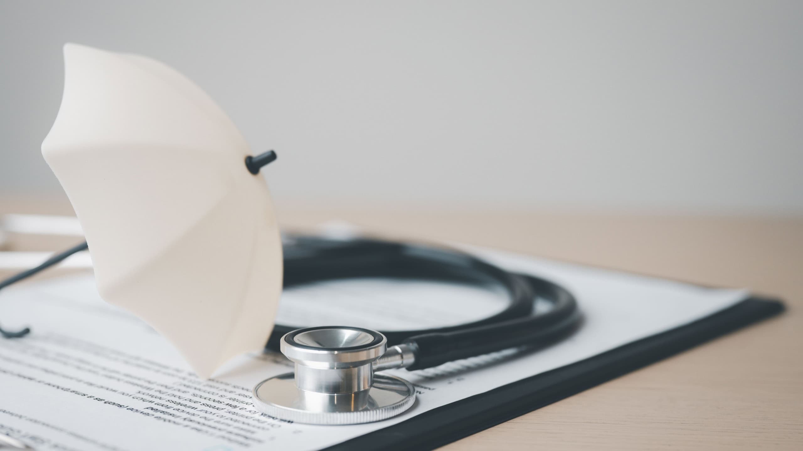 health, insurance, medical, policy, coverage, hospital, A stethoscope and a small umbrella placed on a health insurance document, symbolizing medical coverage, protection, and healthcare policy.