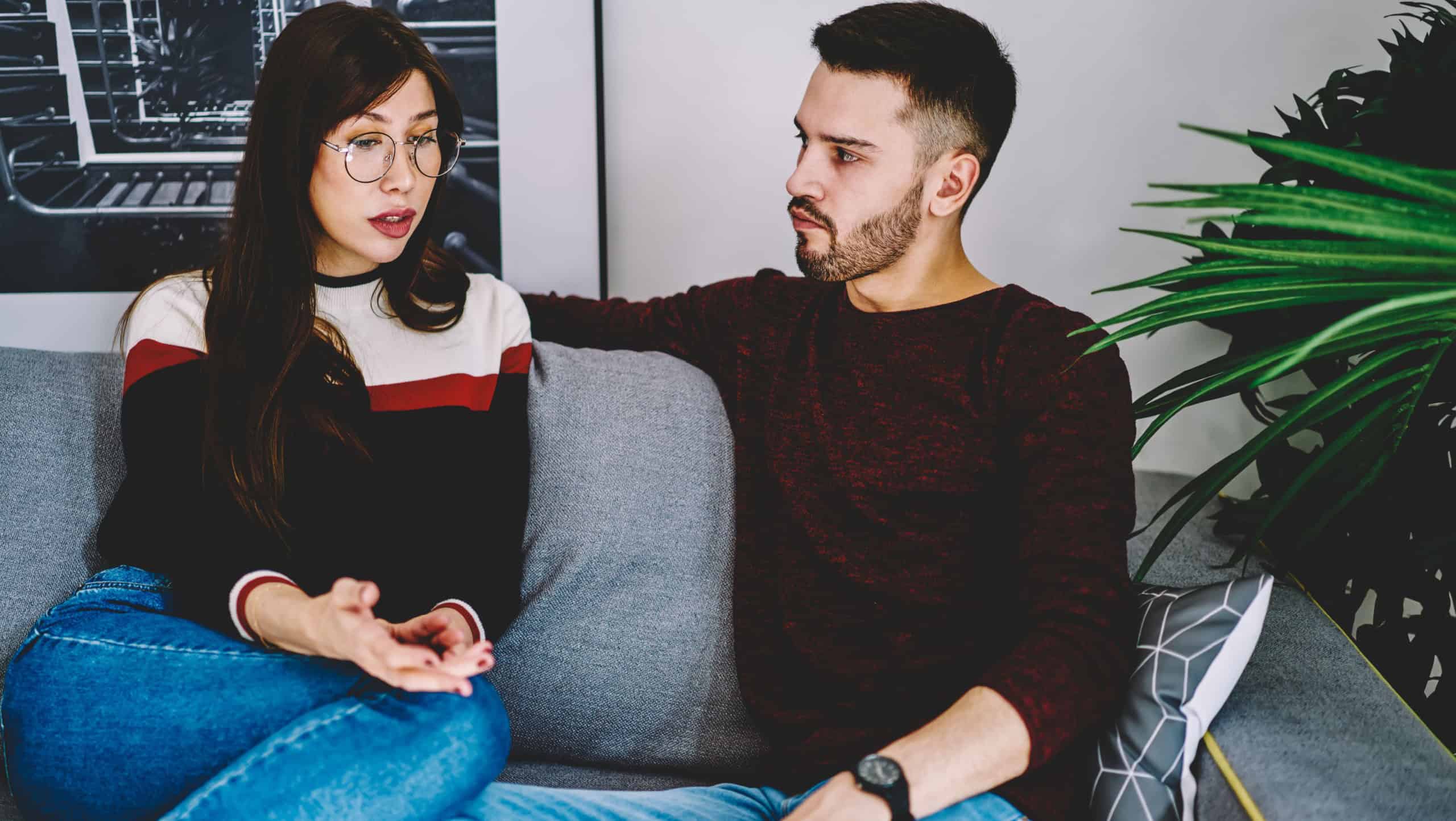 Serious husband and wife concentrated on solving problems of their marriage during leisure time on comfortable sofa in living room, girlfriend and boyfriend have discussion during dispute at home