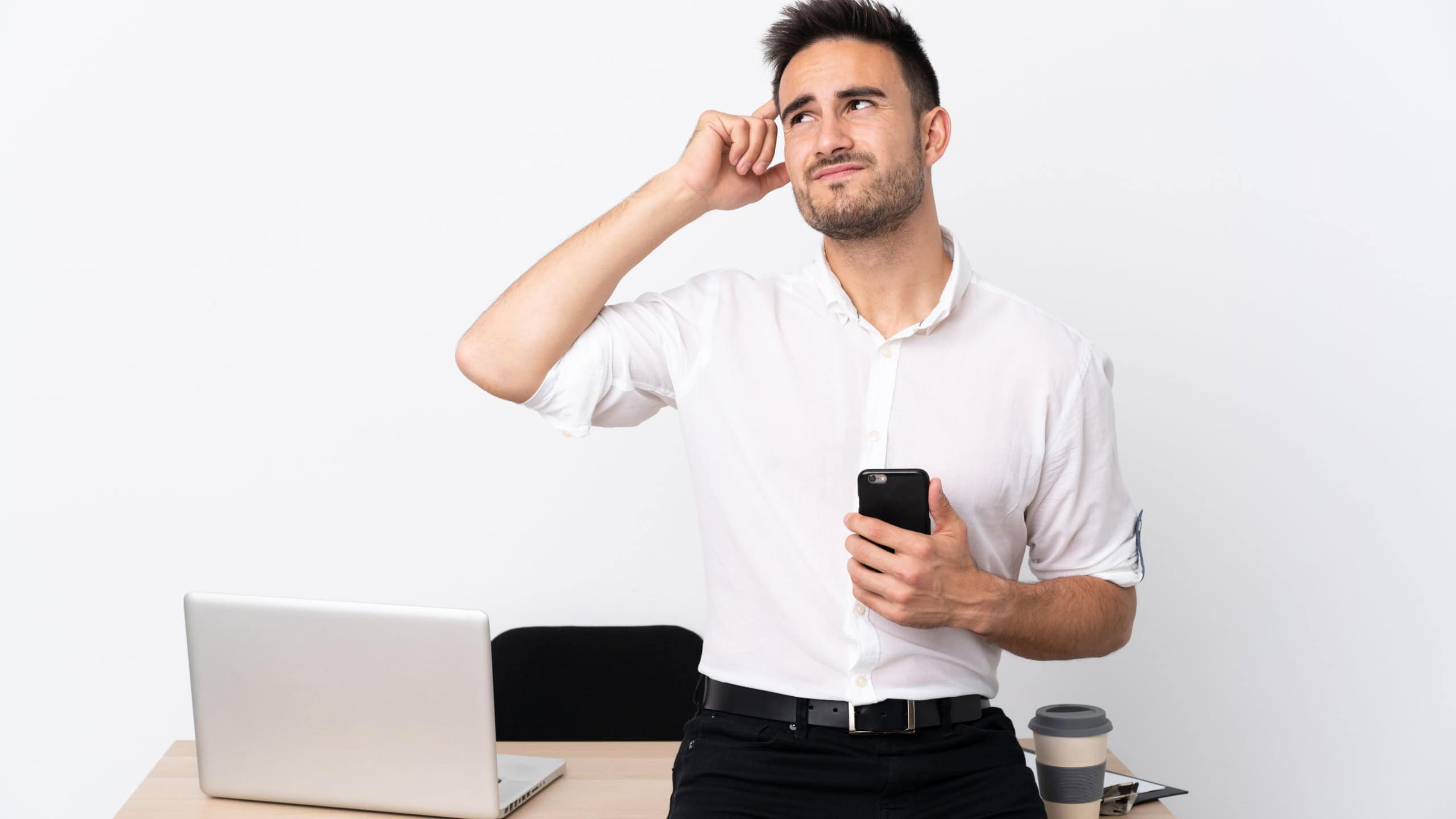 Young business man with a mobile phone in a workplace having doubts and with confuse face expression