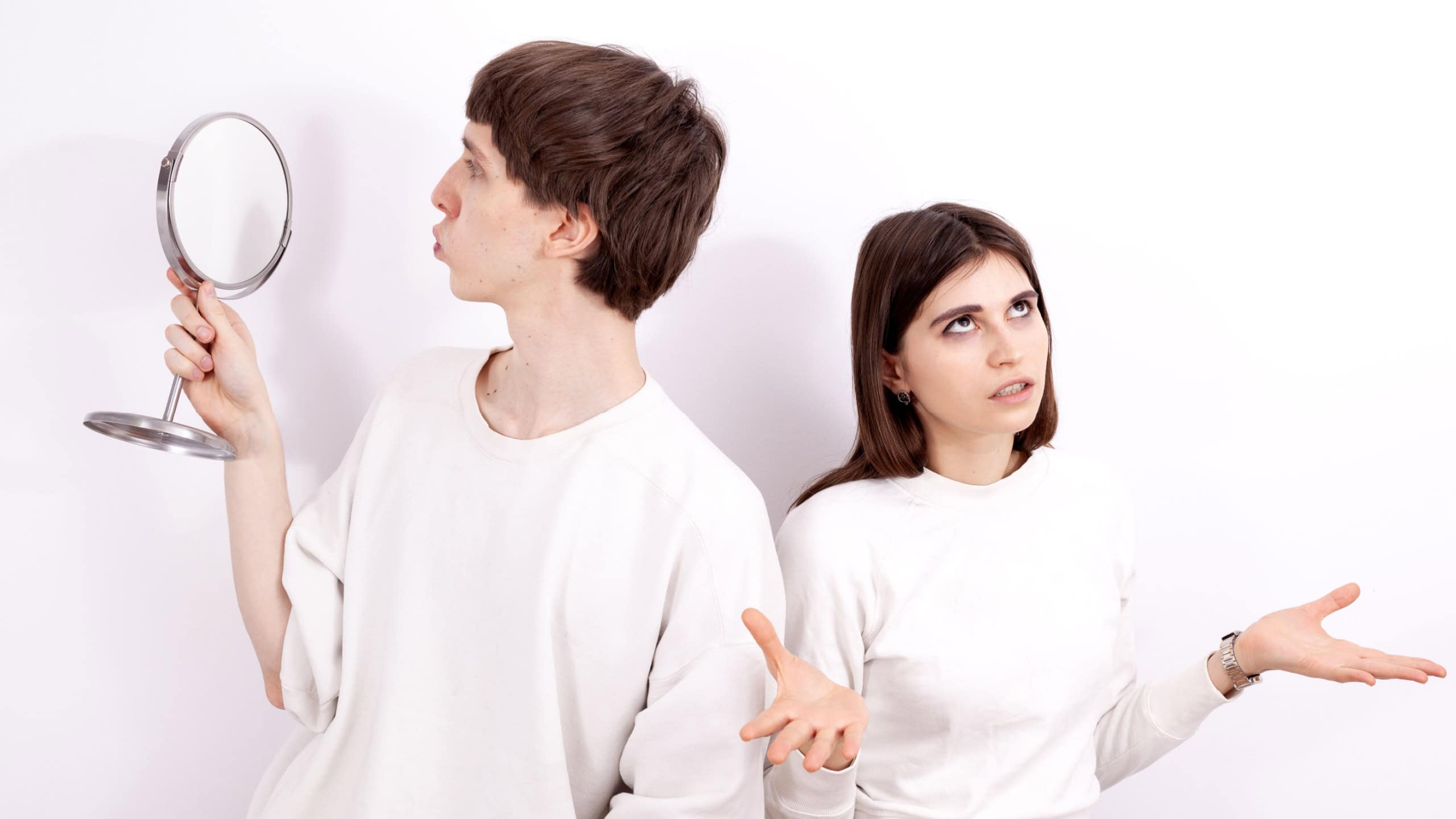 The narcissistic young man in a white sweatshirt is looking at the mirror. He is concentrated on himself and ignoring the young girl standing next to him.
