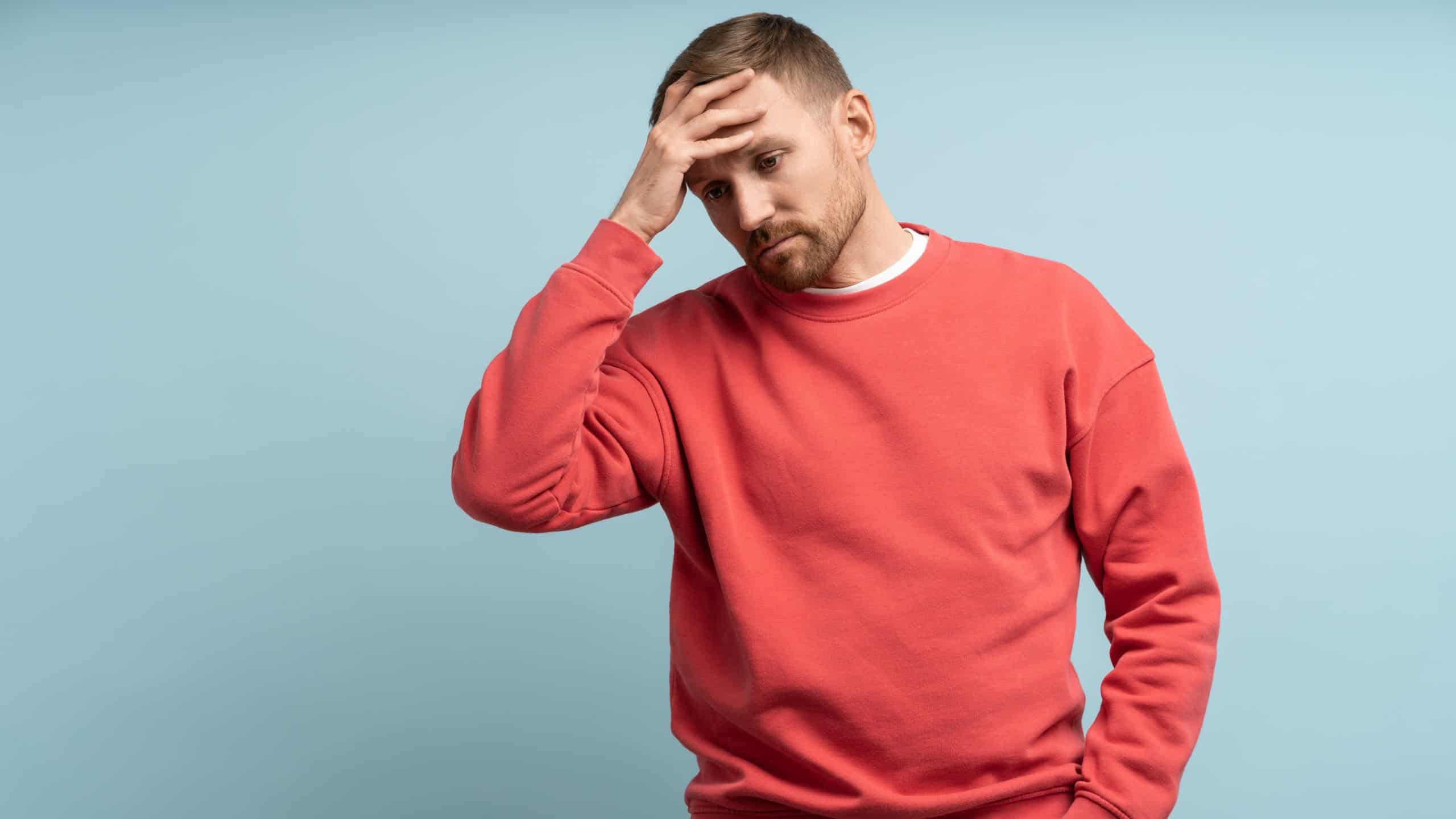 Worried man feeling heartbroken and stress put hand to forehead. Middle aged male isolated on studio blue background with expression of anxiety, detachment, shock, alienation, disappointment on face.