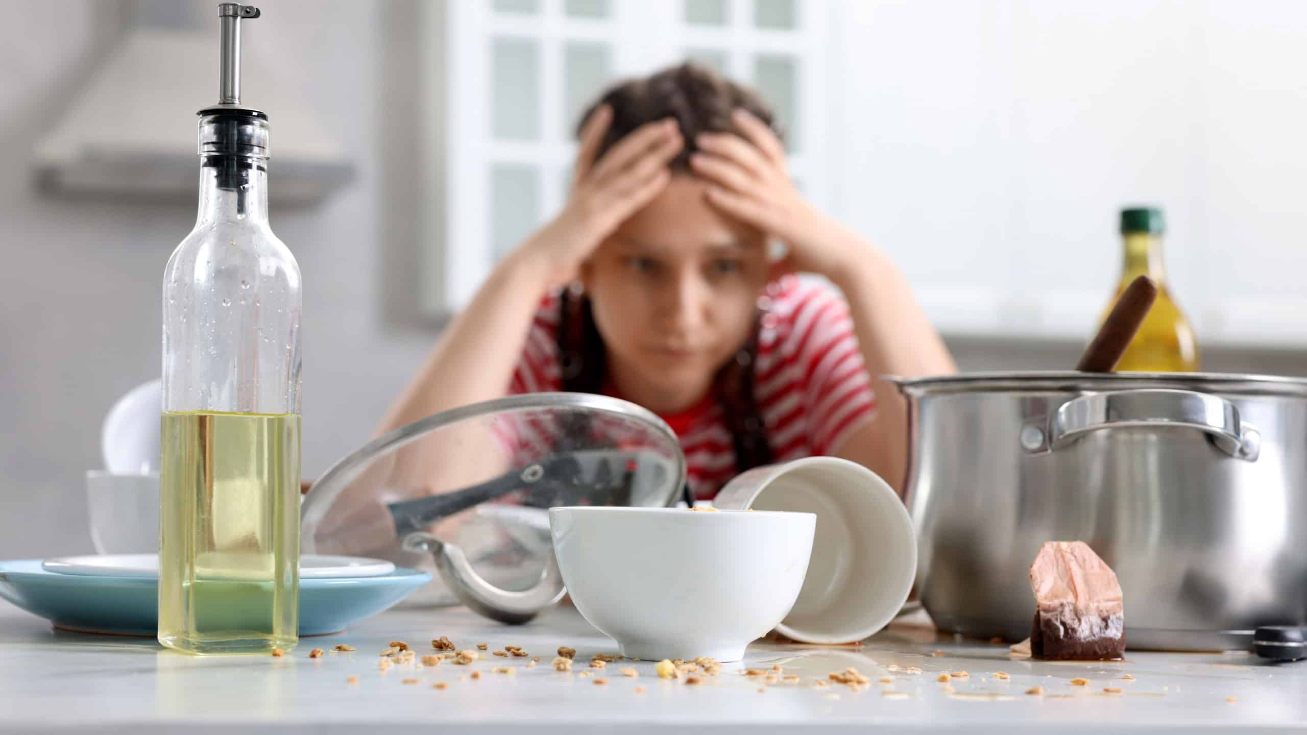 Stressed woman in messy kitchen. Many dirty dishware and utensils on table
