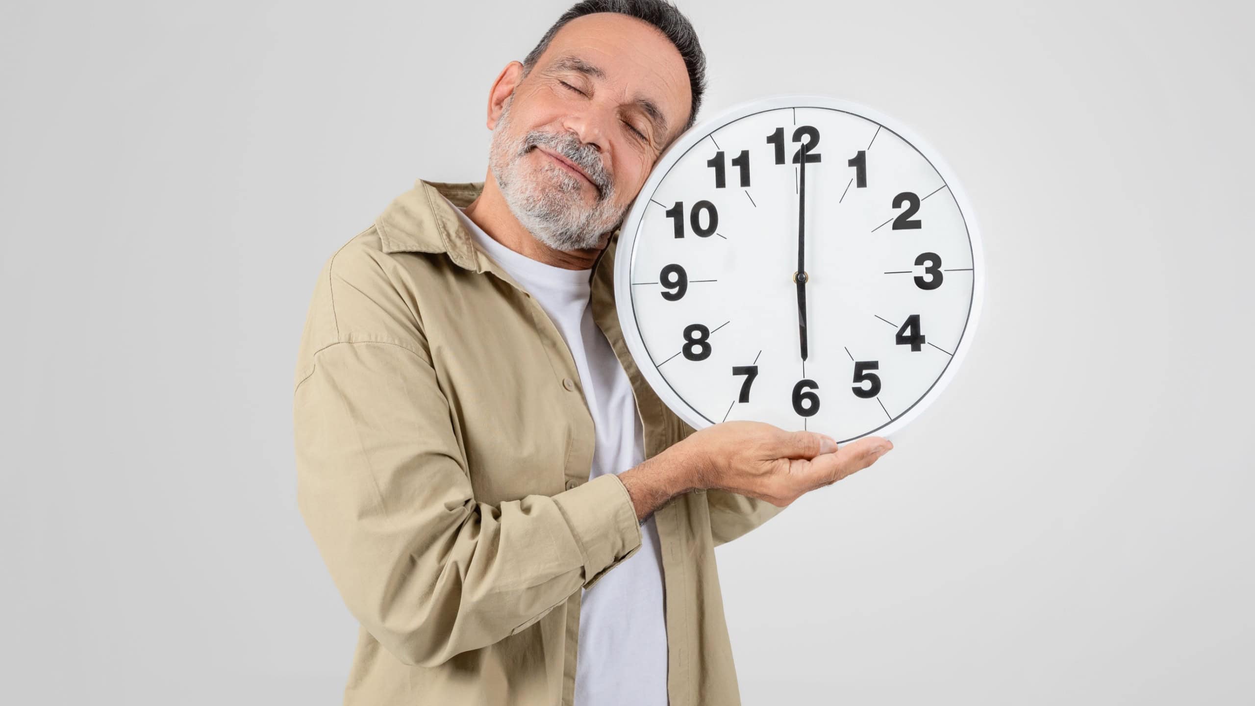 An older man holding a large clock in front of him, isolated on a white background, symbolizes the concept of time and aging
