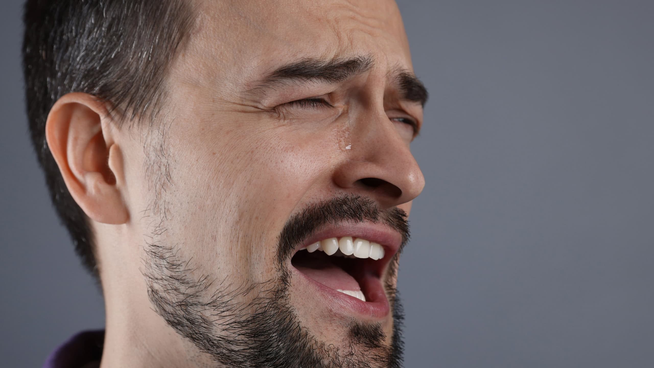 Sad man crying on grey background, closeup. Space for text