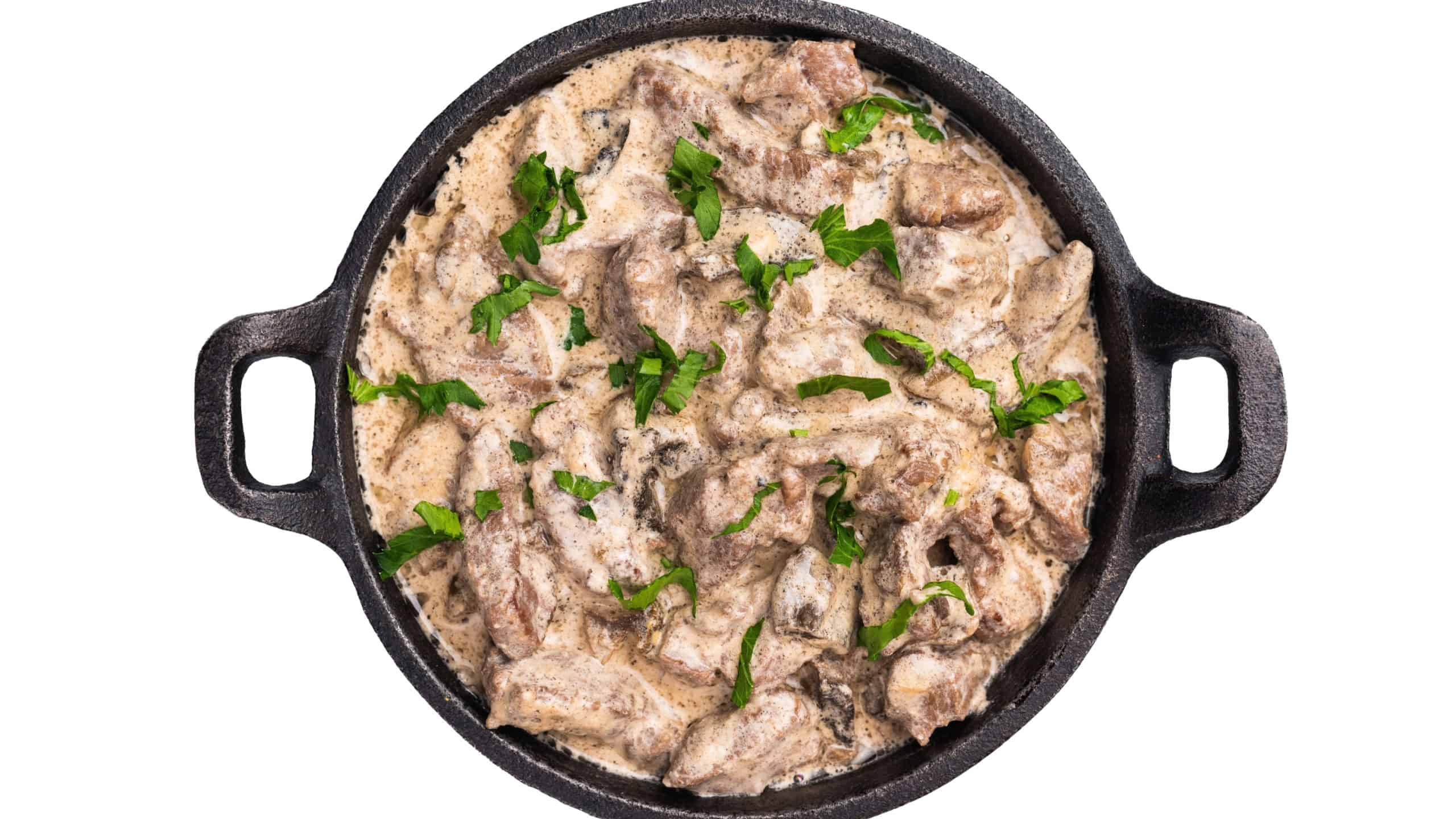 Creamy beef stroganoff with fresh greenery in a skillet isolated on white background. top view.