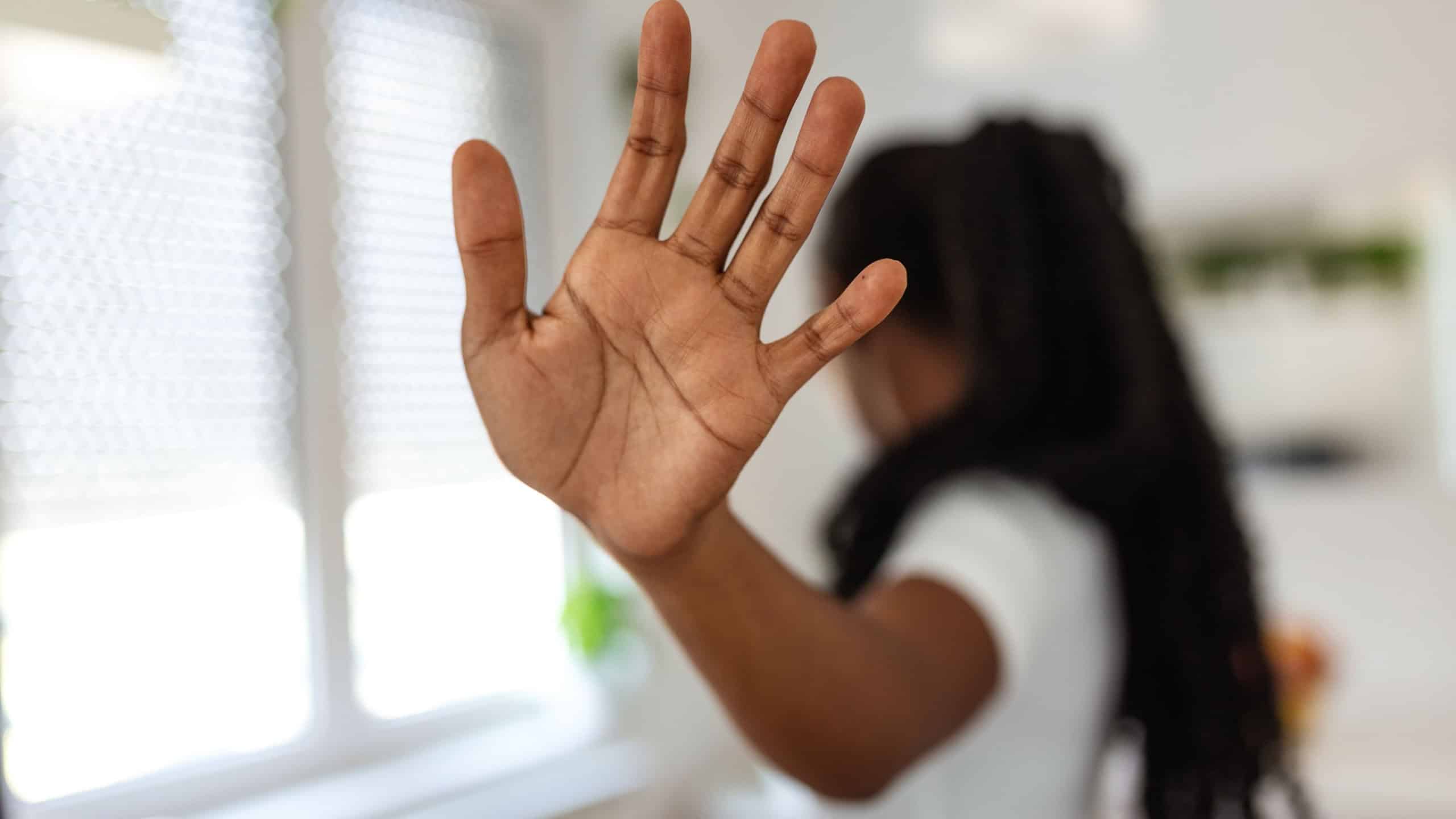 Hand of a Black woman showing stop gesture, expressing refusal and setting boundaries. Concept of saying no, harassment prevention, and personal space on a grey background.