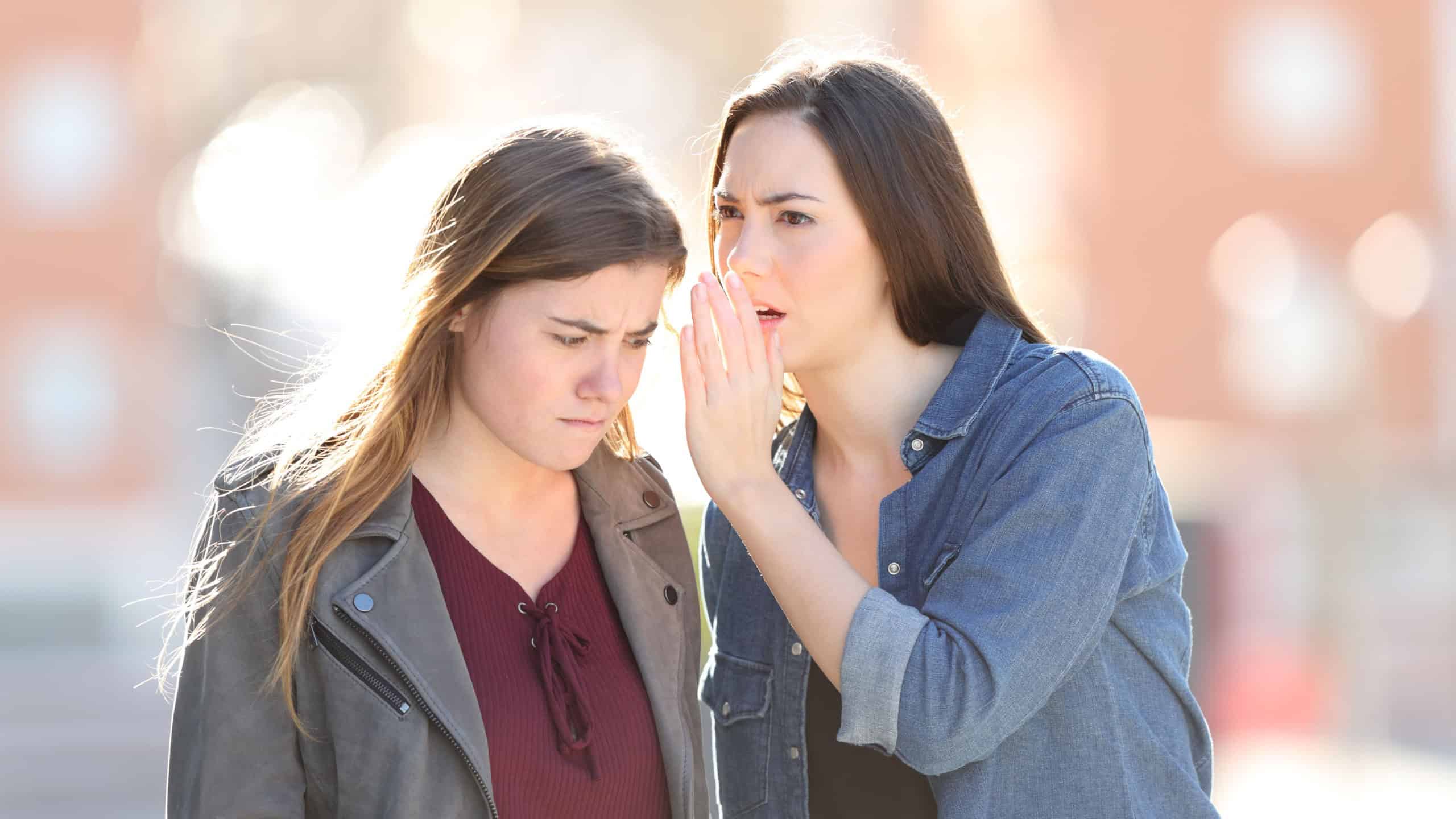 Gossip woman telling secret to her angry friend in the street
