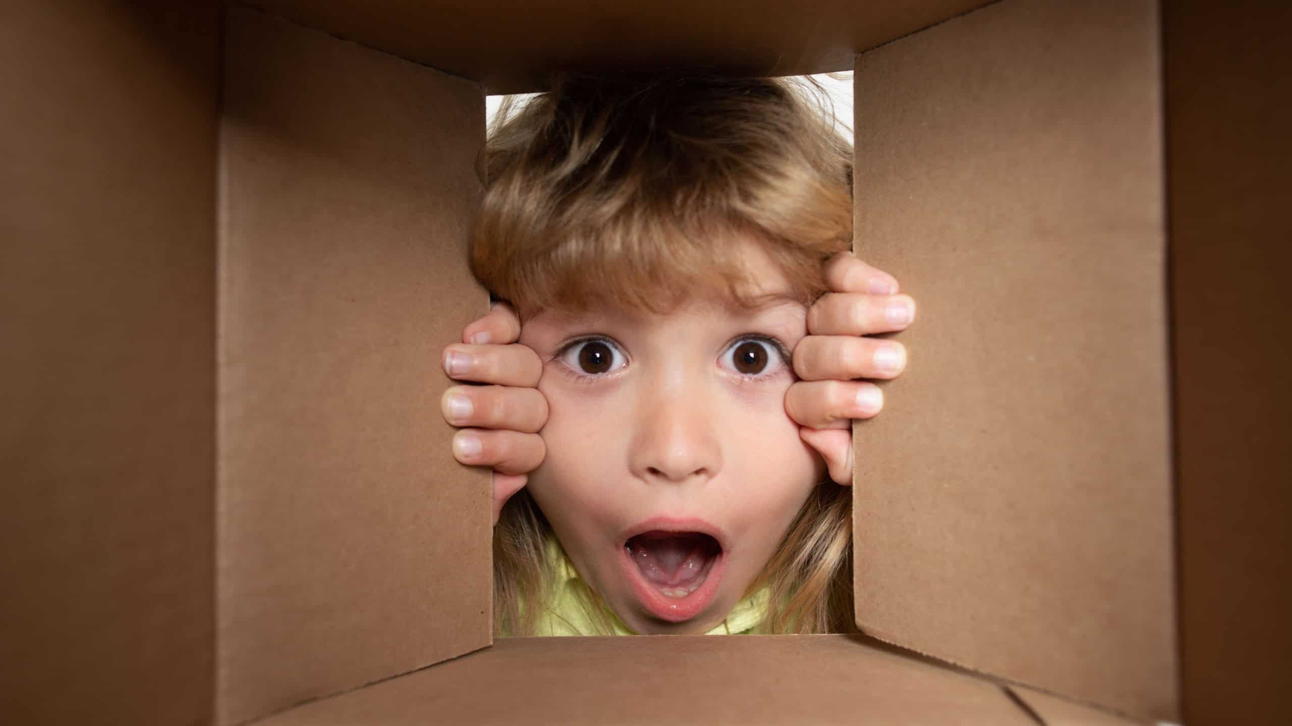 Kid open paper cardboard box. Child open carton delivery box, packaging open and closed cardboard box. Closeup kids face.