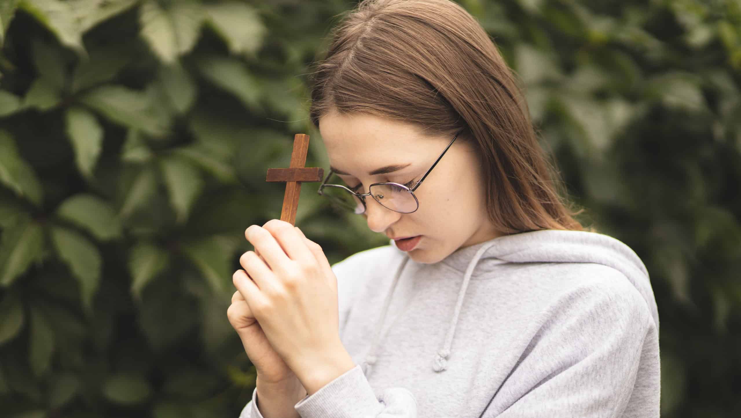 Close-up of hands on the Bible. The process of prayer. The girl holds a wooden crucifix in her hands and prays. Woman's prayer.