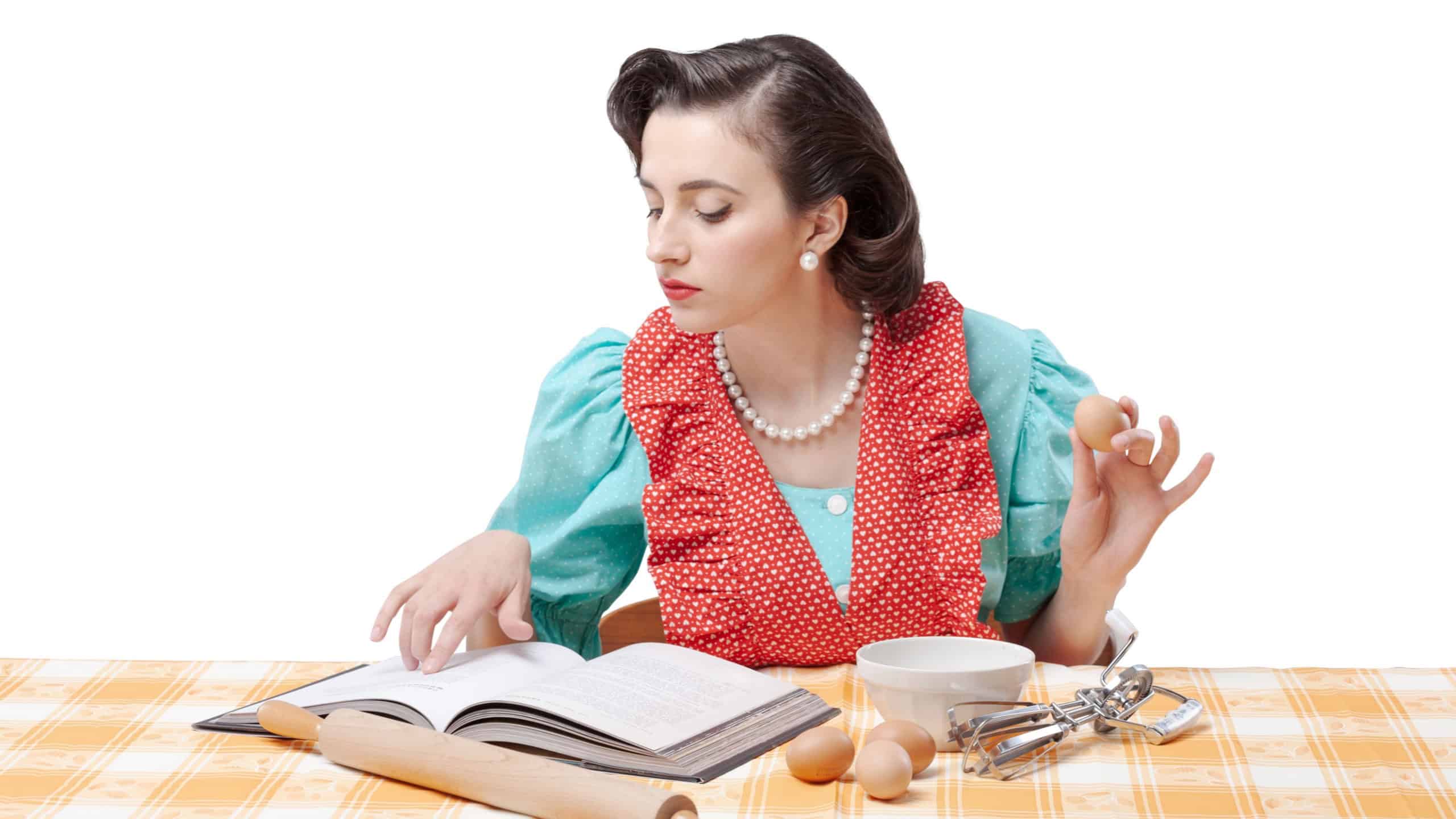 Beautiful vintage style housewife preparing a dessert at home, she is checking the recipe in a cookbook and mixing ingredients in a bowl