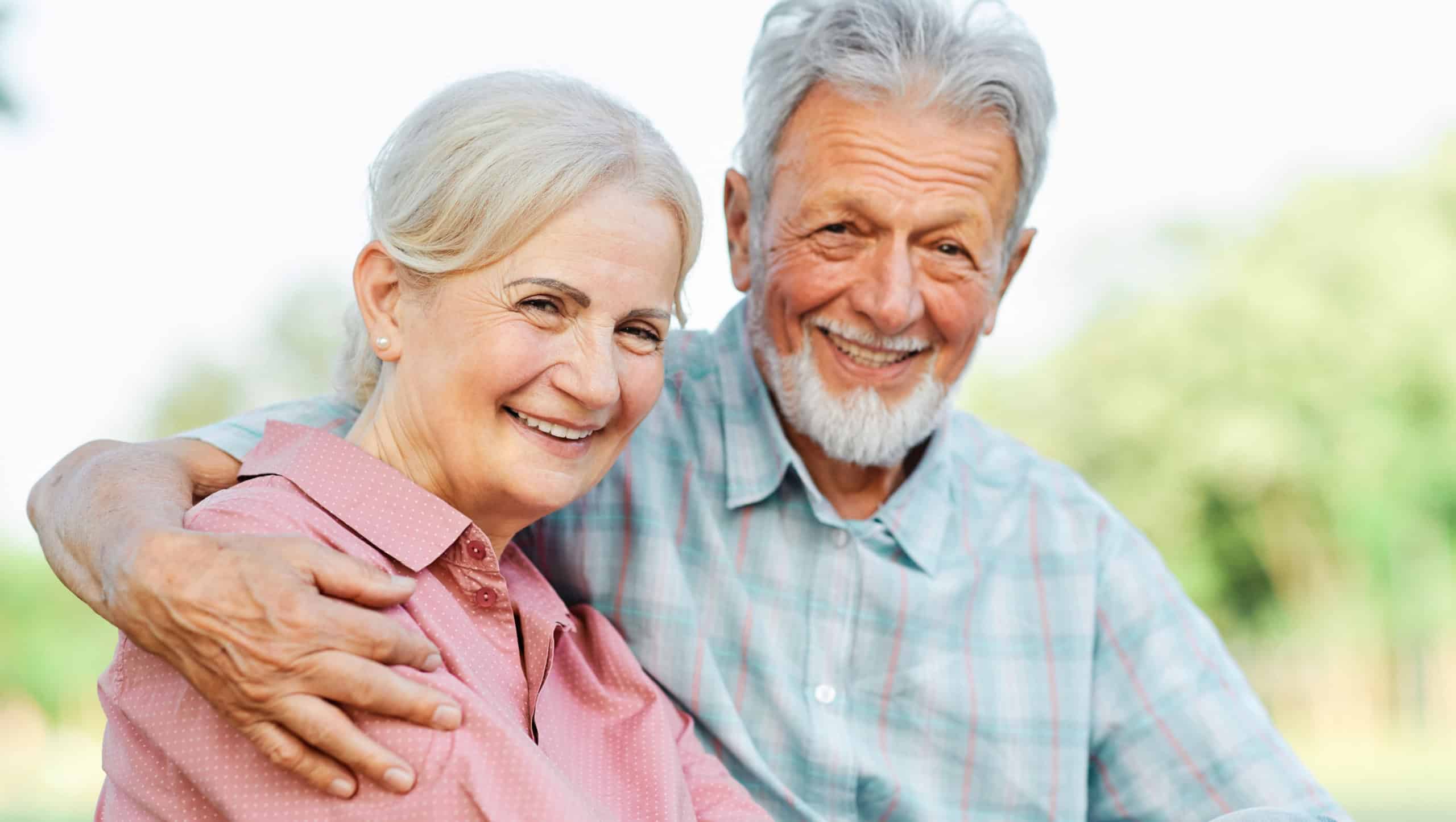 Happy active senior couple having fun talking and hugging sitting on a bench in park outdoors
