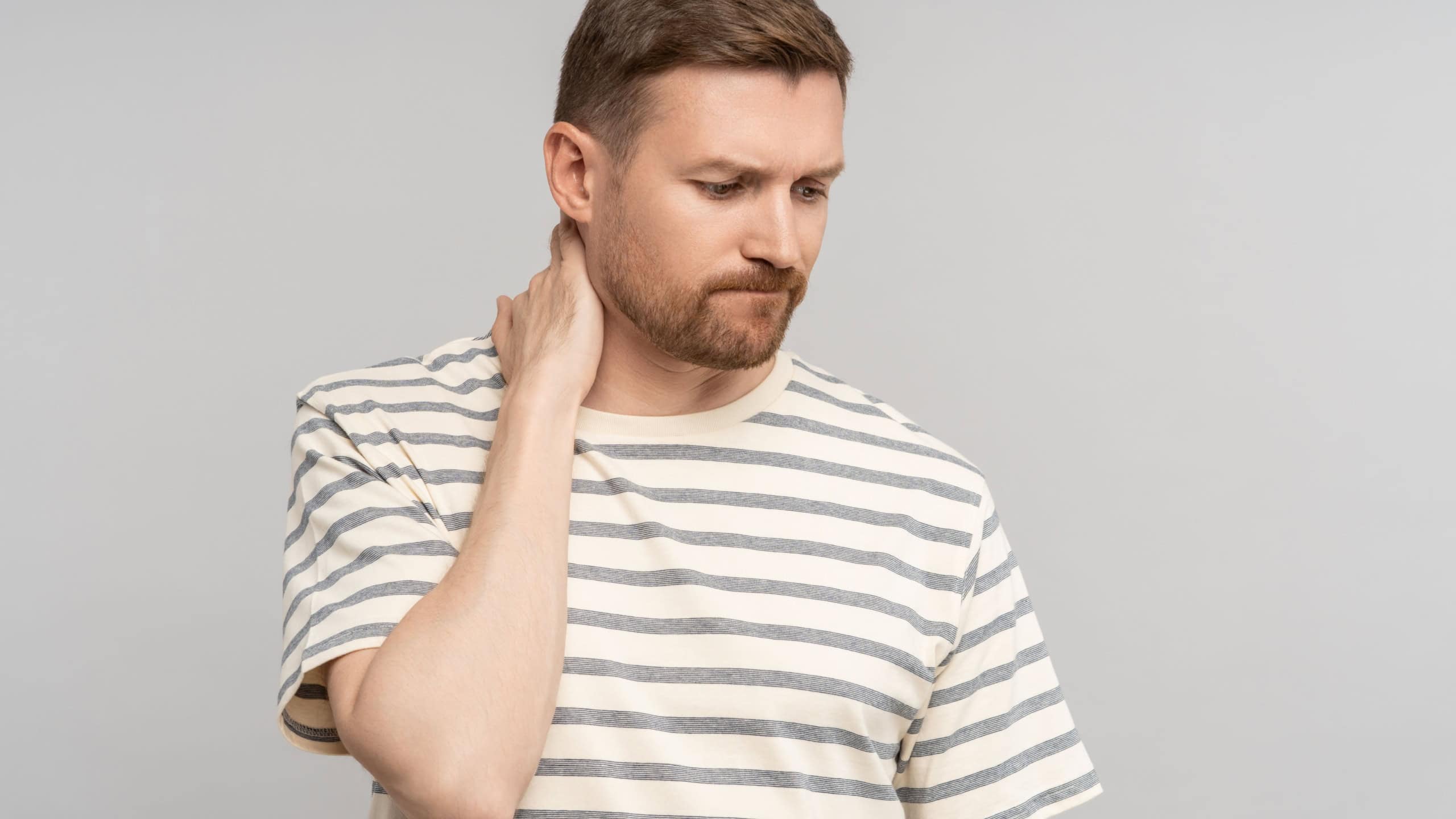 Upset disappointed man suffering from depression with frustrated expression, sense of loss touch neck. Emotional stressed guy sadly looks down thinking about failure, life trouble, isolated background
