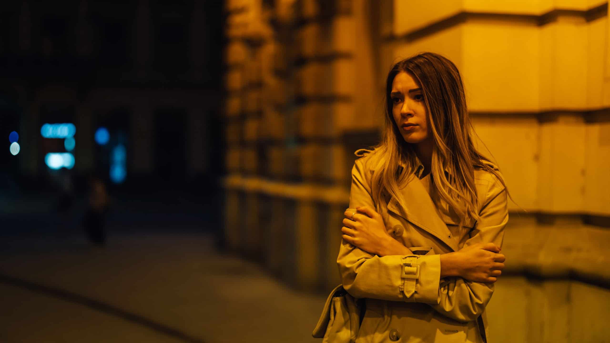 Portrait of a sad and worried woman walking down the streets of a city during night and not feeling safe to be alone.