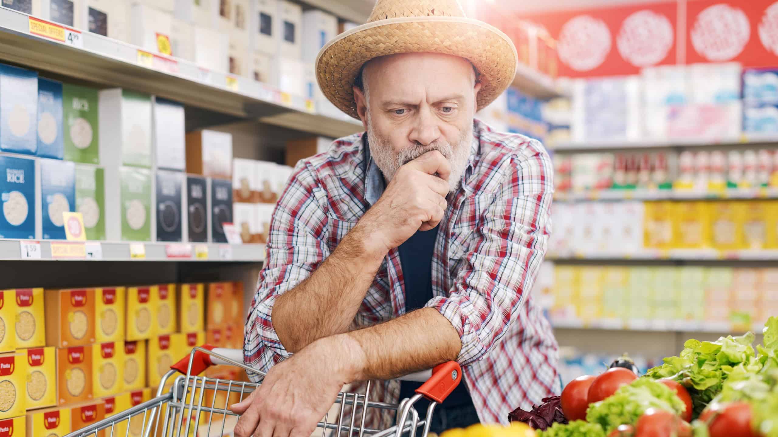 Picky farmer buying fresh vegetables at the grocery store, he is looking at the vegetables and thinking