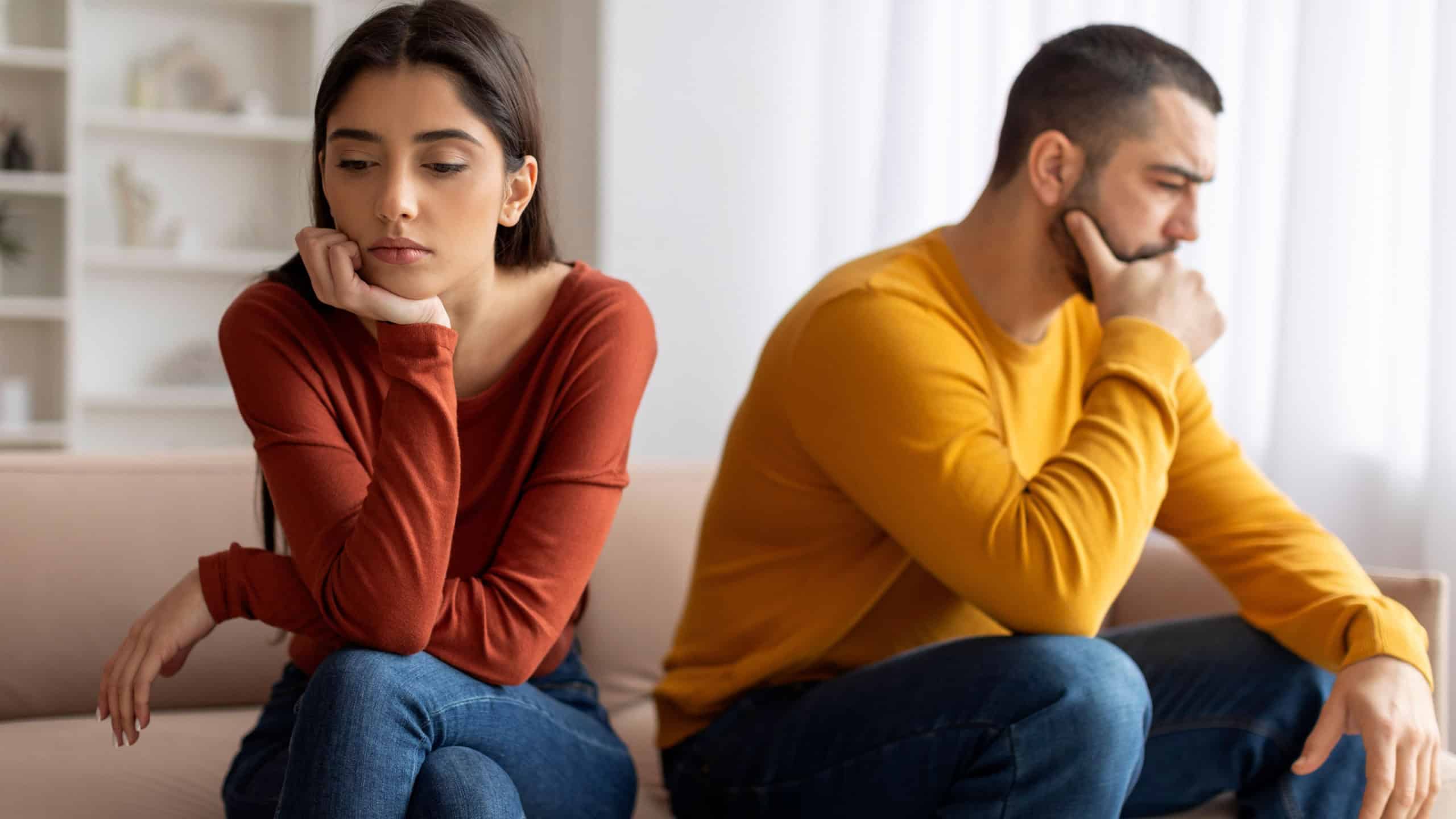 Upset Young Man And Woman Offended To Each Other After Argue At Home, Pensive Millennial Spouses Sitting On Couch With Thoughtful Face Expression, Suffering Relationship Crisis After Domestic Quarrel