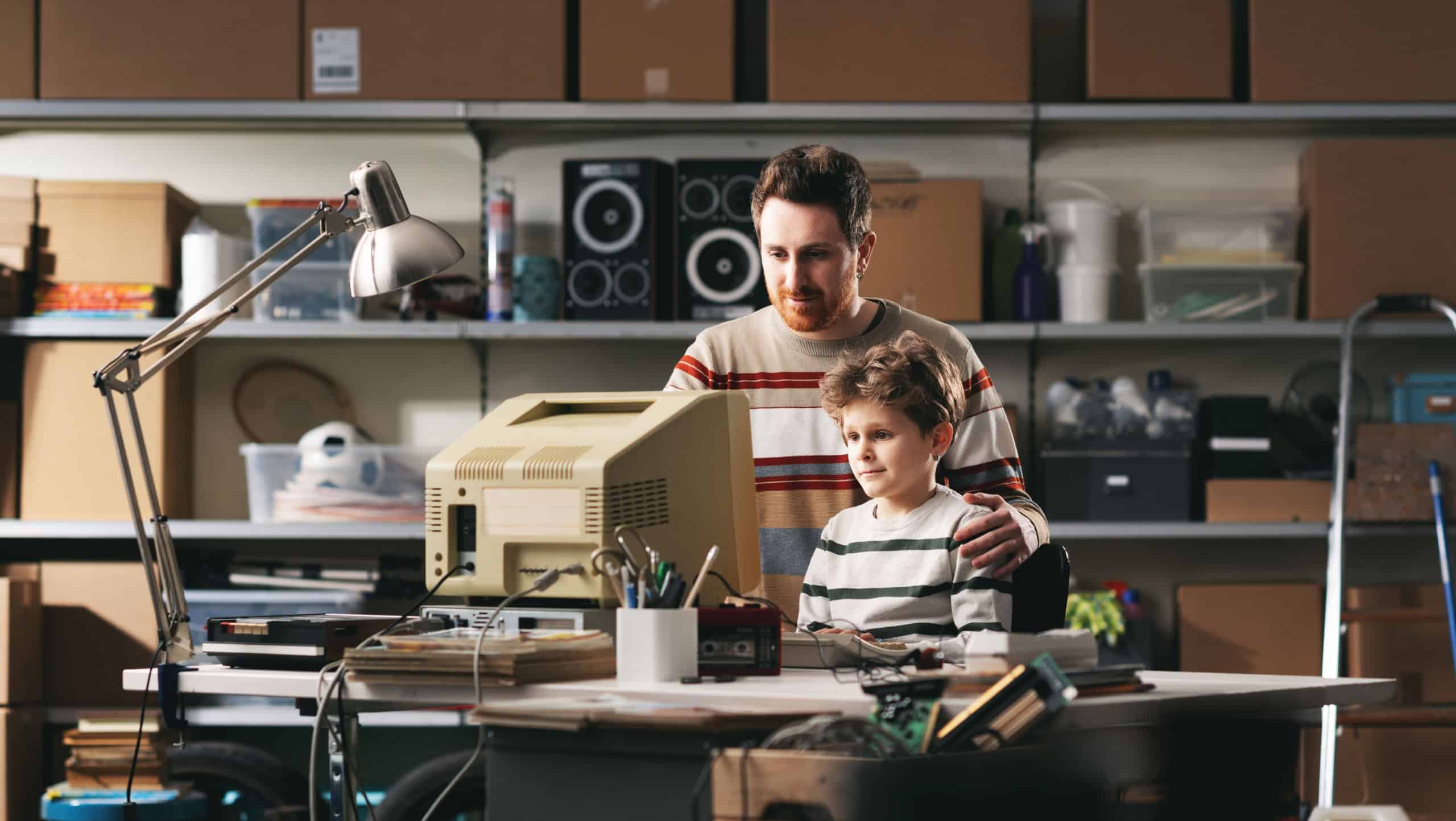 Father and son using an old PC in the garage, he is teaching him how to use a computer