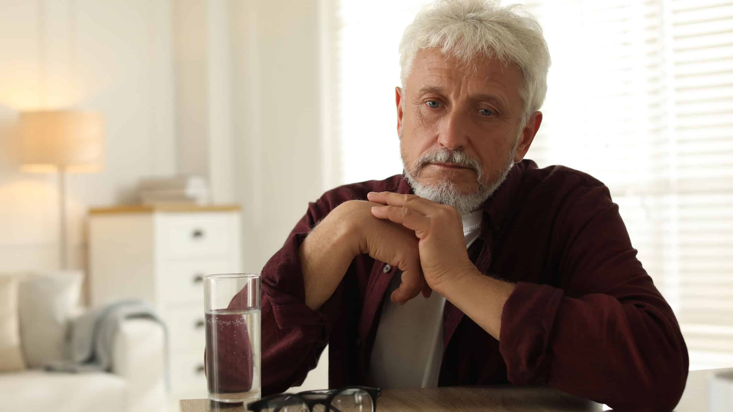 Sad senior man feeling lonely while sitting at wooden table indoors