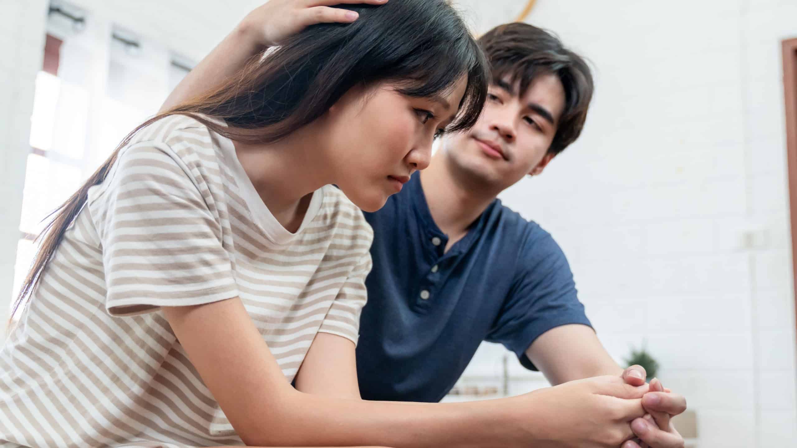 Asian young husband comforting his wife crying with tears for problem. Attractive man support, consoling and understand empathy to depressed stressed woman in bedroom at home. Family relationship.