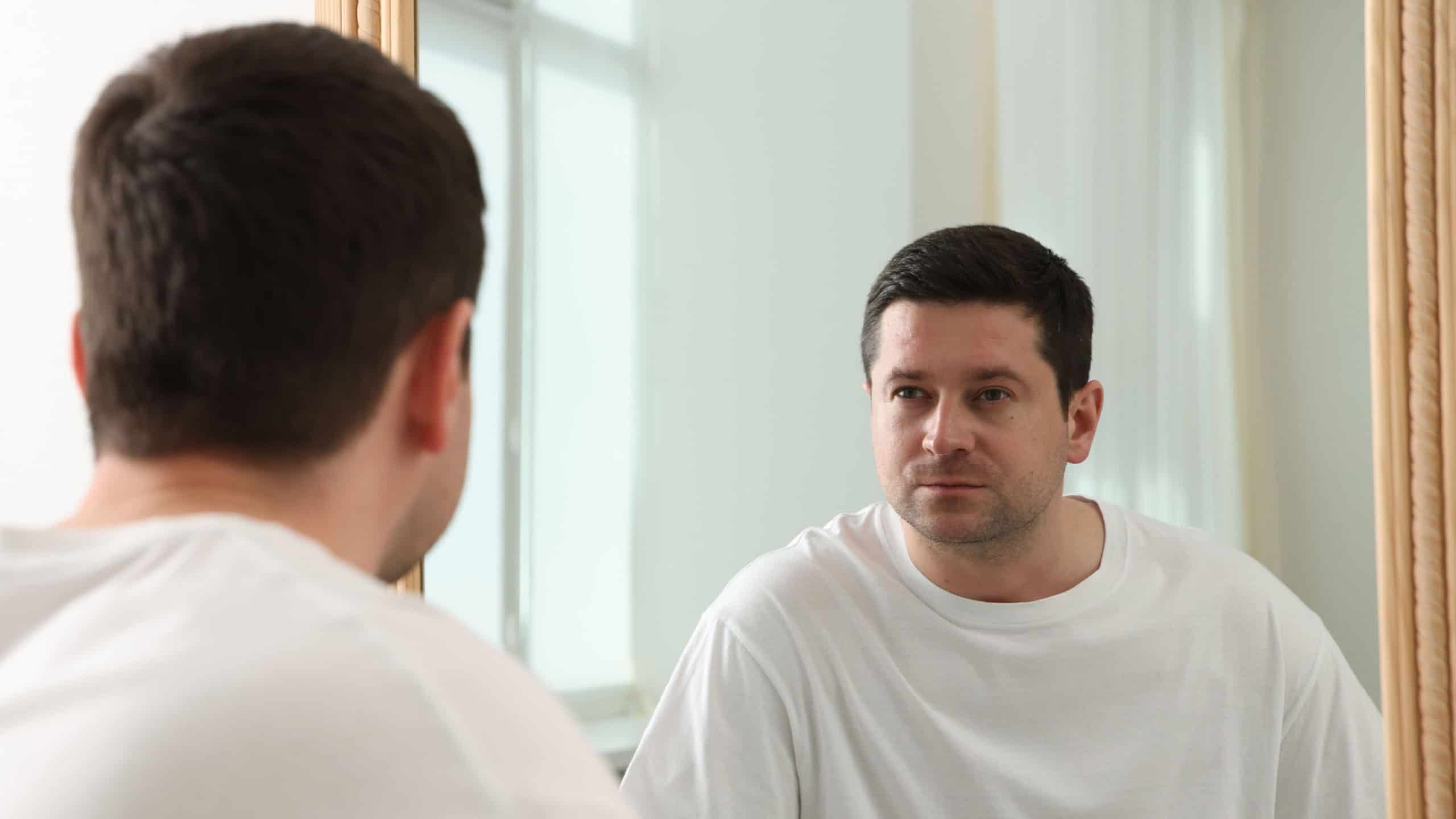 Handsome man looking at himself in mirror indoors