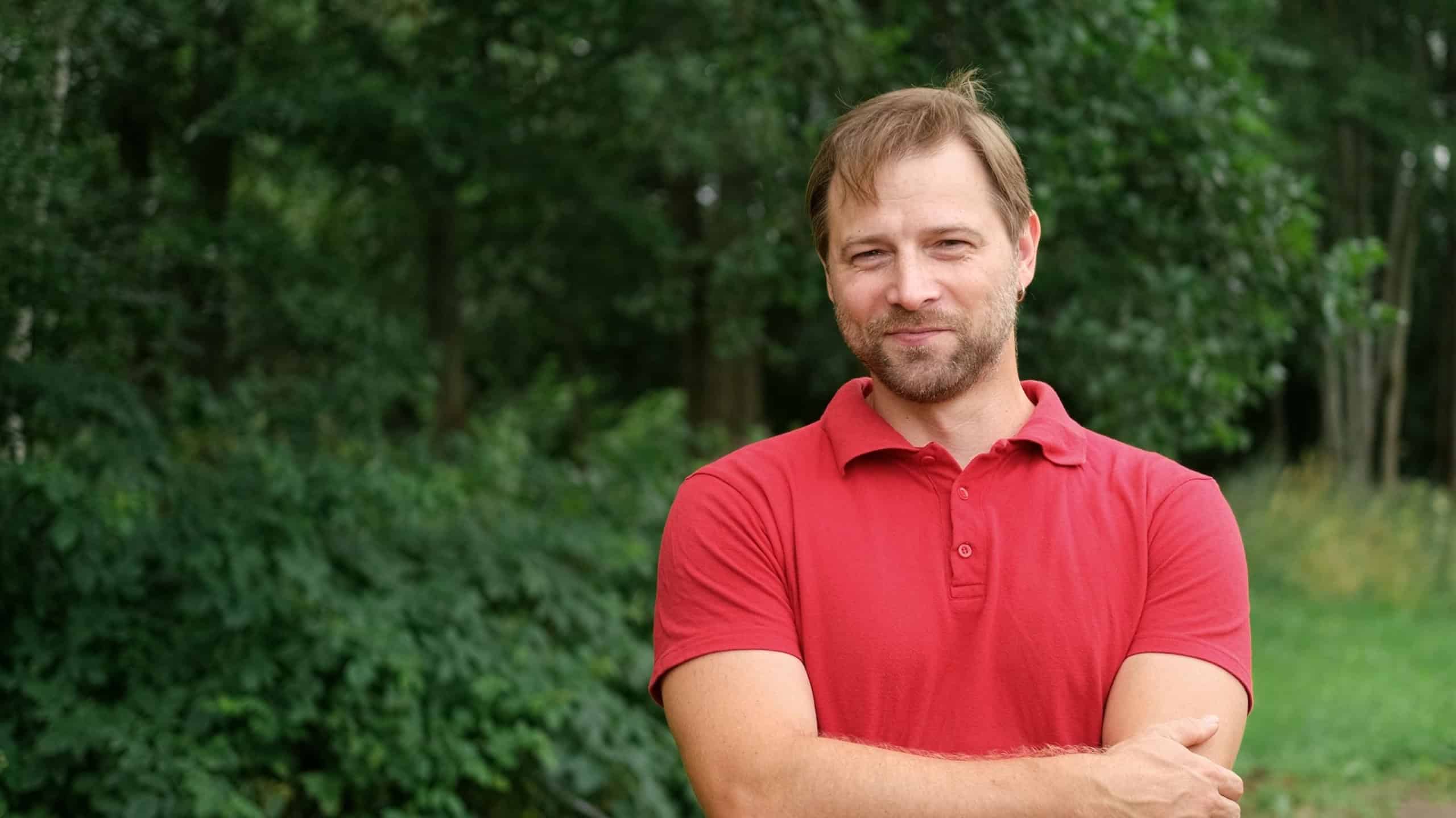 Portrait of handsome young man in orange t-shirt outdoors. Male with long hair and beard feel happy, calm and serious on Green nature background. Man looking away into distance. Diversity People.