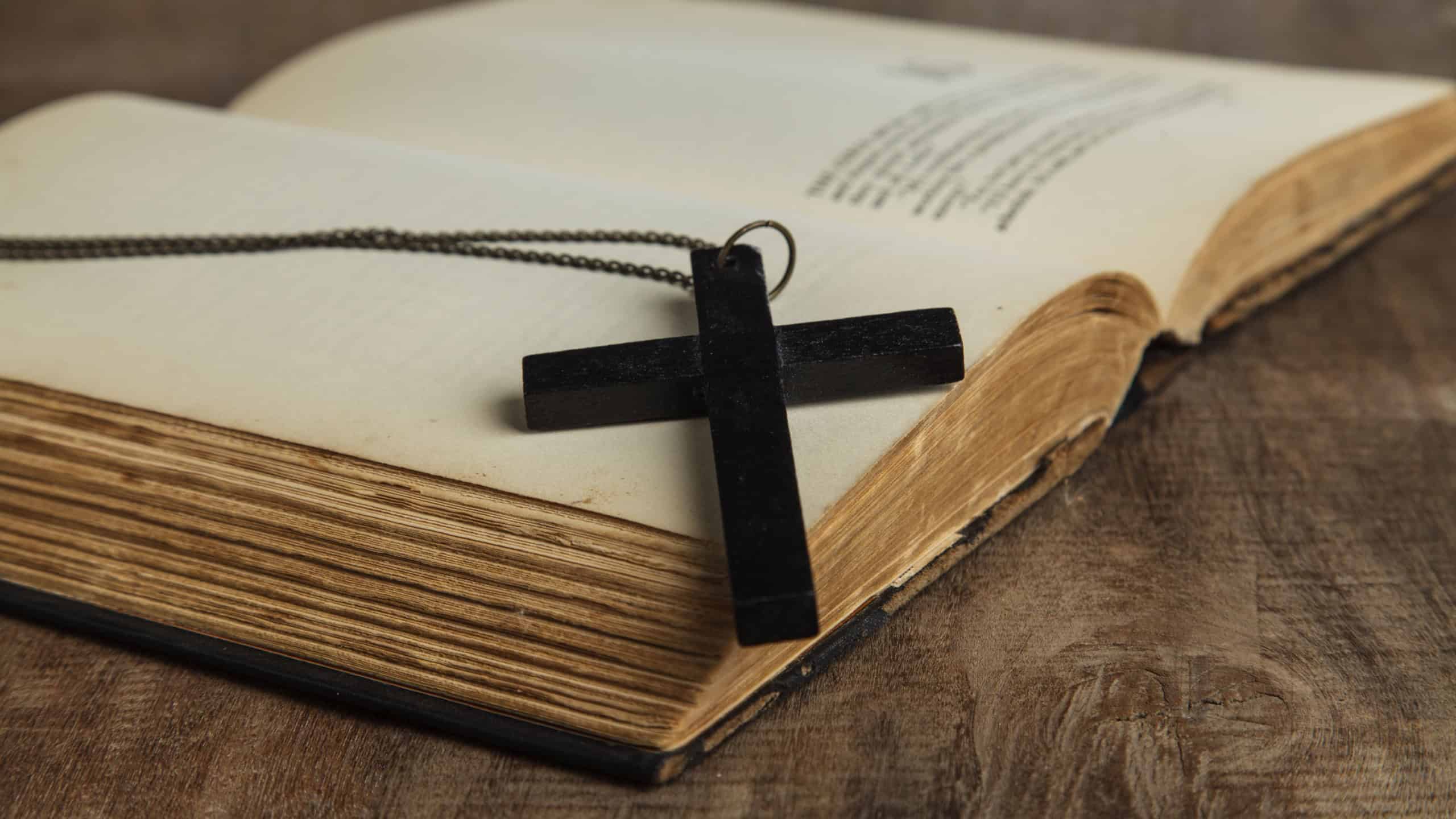 Cross over wood table with old book, holy Bible