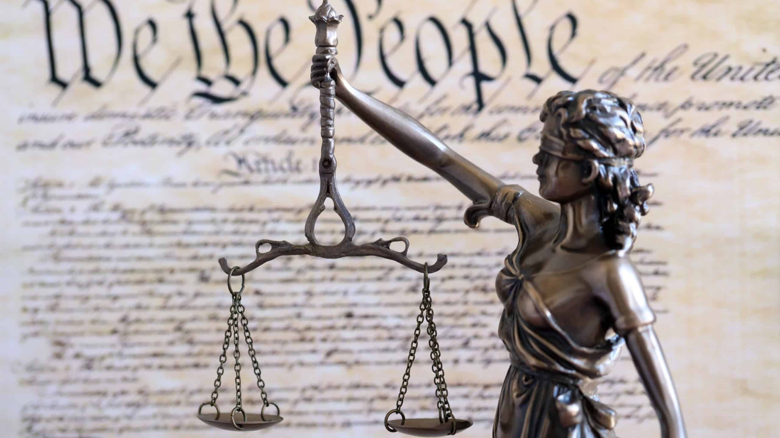 Lady Justice statue with scales on background of US Constitution page close up. Lawsuit and punishment in United States