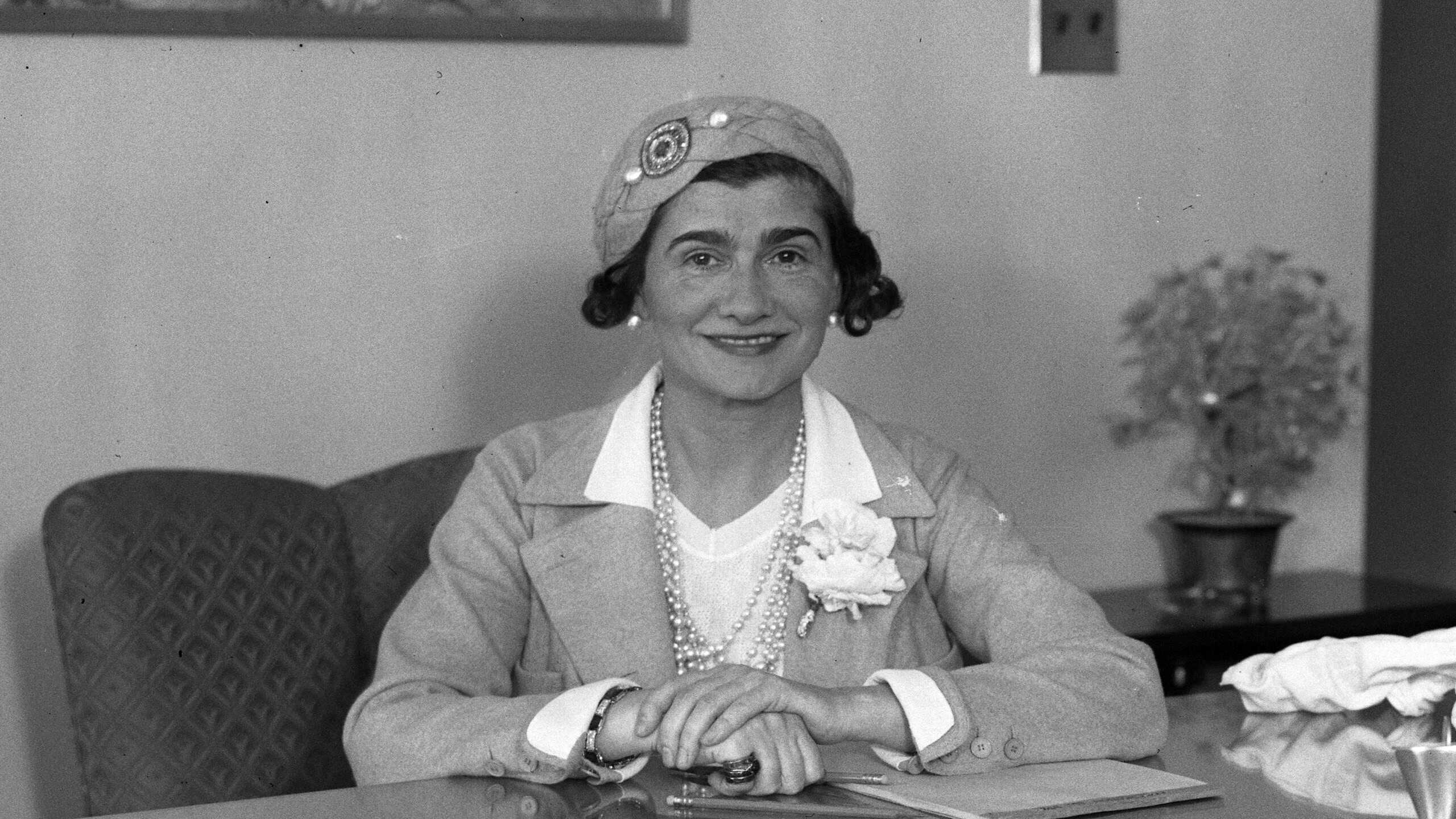 Coco Chanel sitting at a desk during a visit to Los Angeles