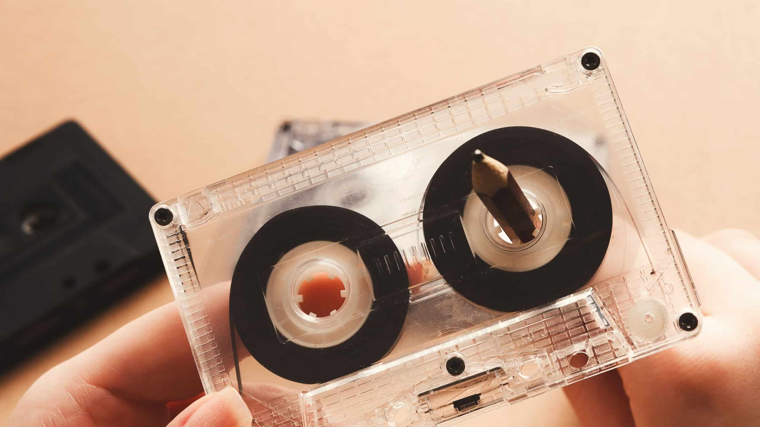 Hands rewinding magnetic tape audio cassette on pencil. Closeup of vintage tape and simple device for rewinding, copy space. Obsolete technology concept