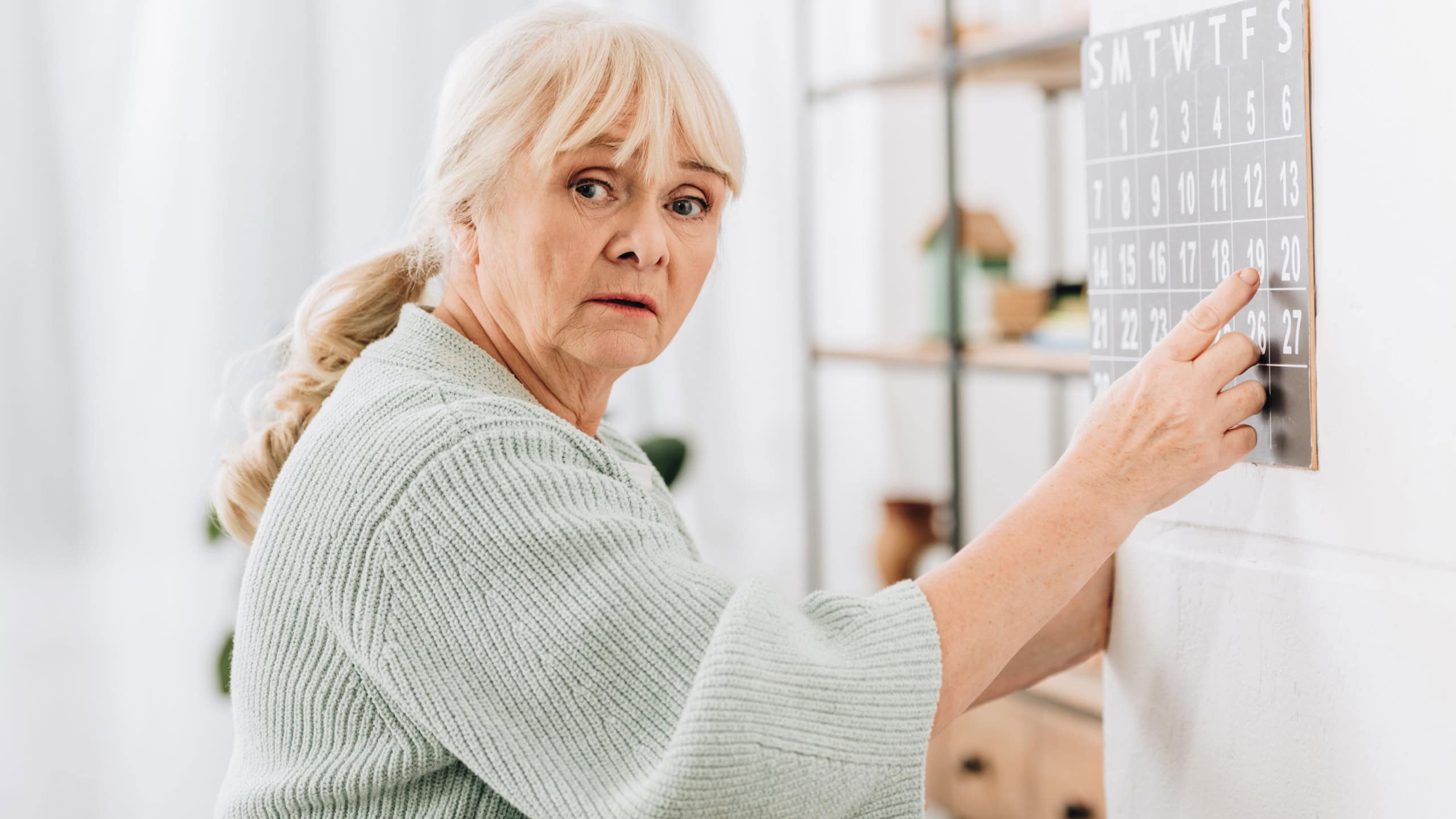 upset senior woman touching wall calendar and looking at camera