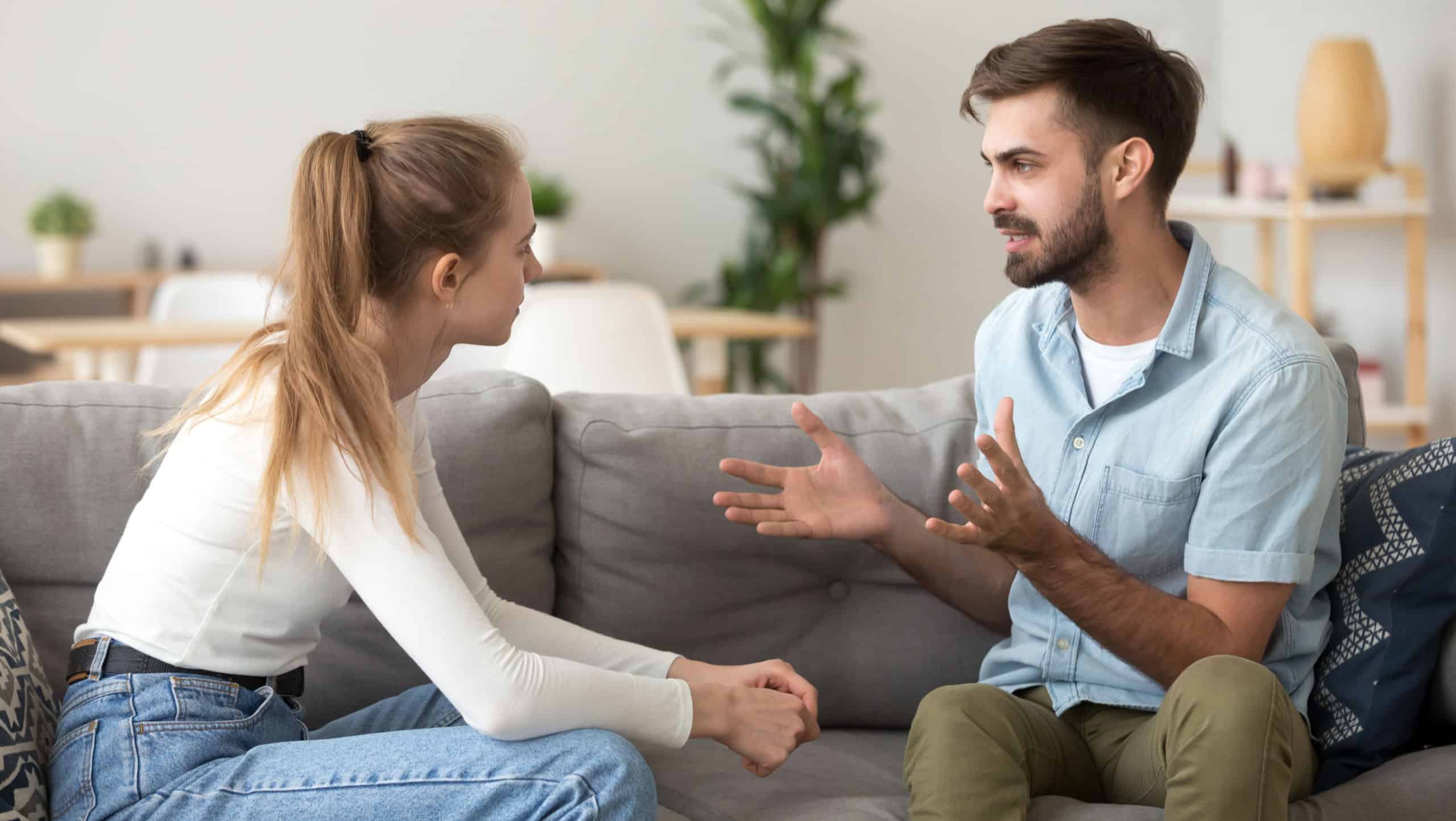 Serious young couple sitting together on sofa, talking about relationships, spending time together at home, focused wife listening to speaking husband, friends having conversation