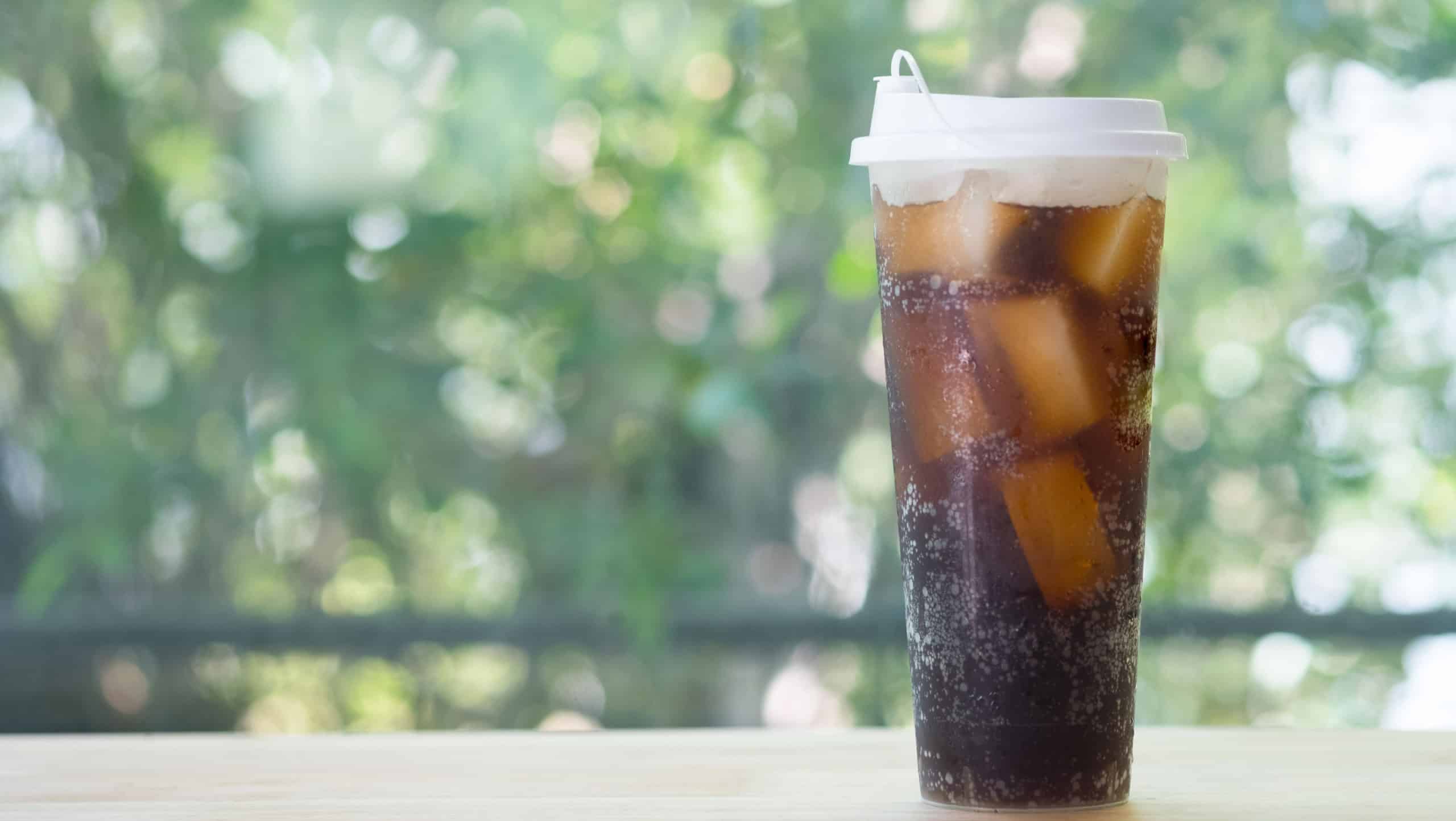 Refreshing black soda soft drinks with ice in a clear plastic tall glass with nature background.