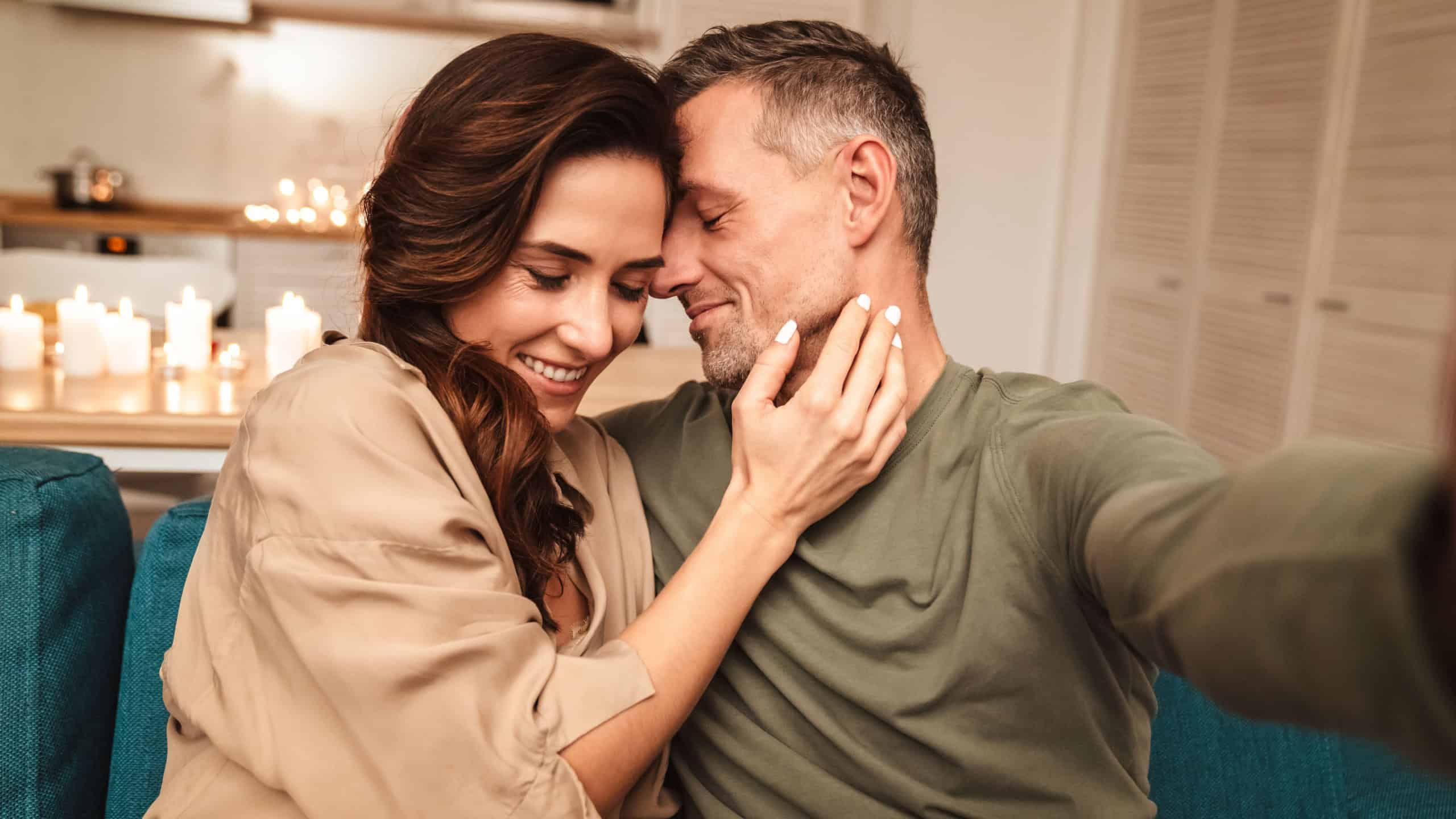 Image of happy caucasian couple taking selfie photo while having romantic candlelight dinner at home