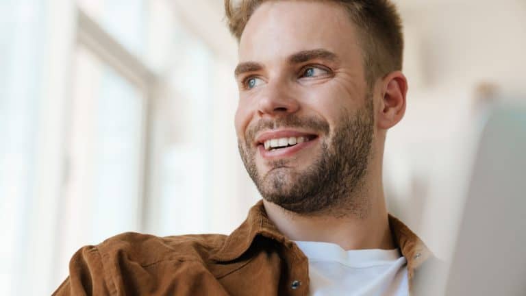 Handsome cheerful guy working with laptop and smiling at home