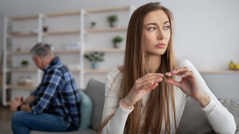 Unhappy mature woman taking off wedding ring, thinking about divorce with her husband indoors, free space. Middle-aged couple going through breakup or separation, having relationship problems