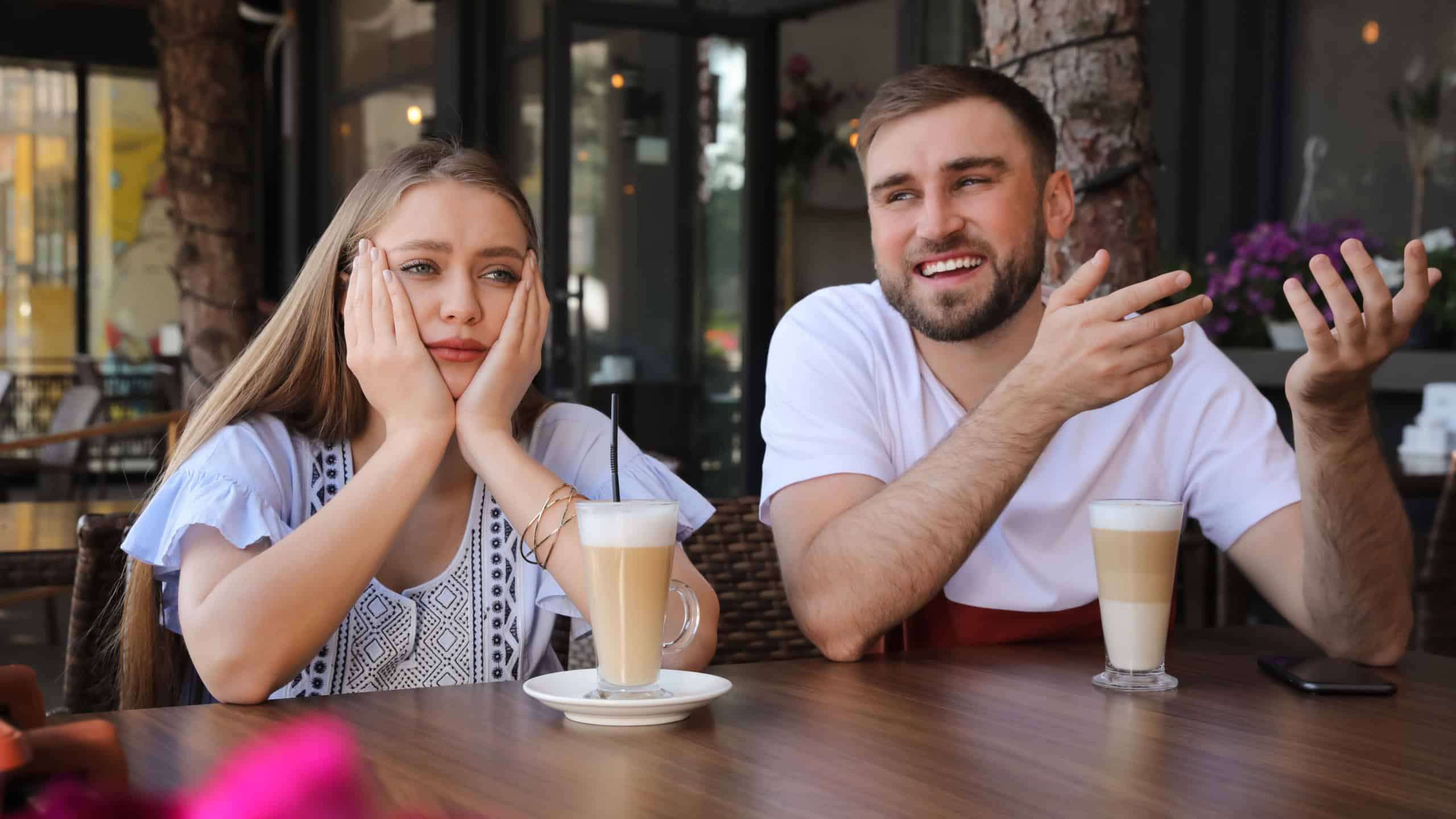 Young woman having boring date with talkative guy in outdoor cafe